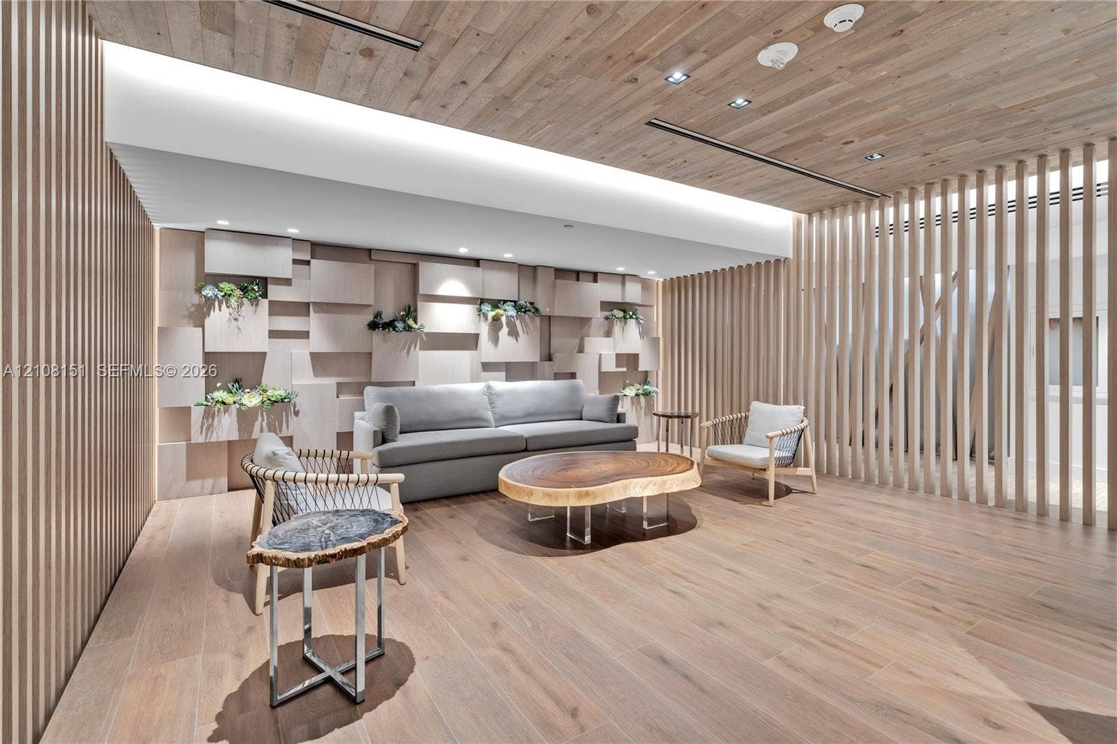 Wood-finish plank flooring, vertical slat wall paneling, ceiling with recessed wood-finish cladding, three-dimensional geometric wall installation, and integrated linear cove lighting