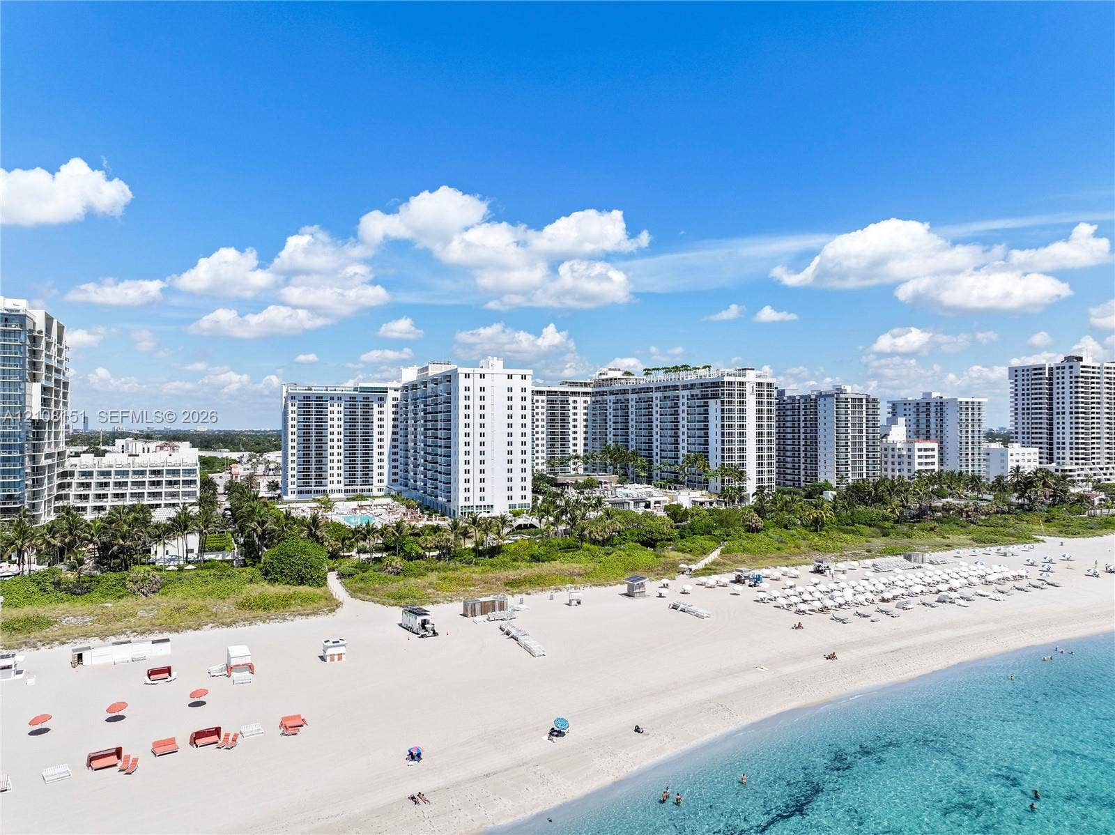 Aerial perspective of coastal high-rise development featuring direct beach access, sandy shoreline, and mature tropical landscaping