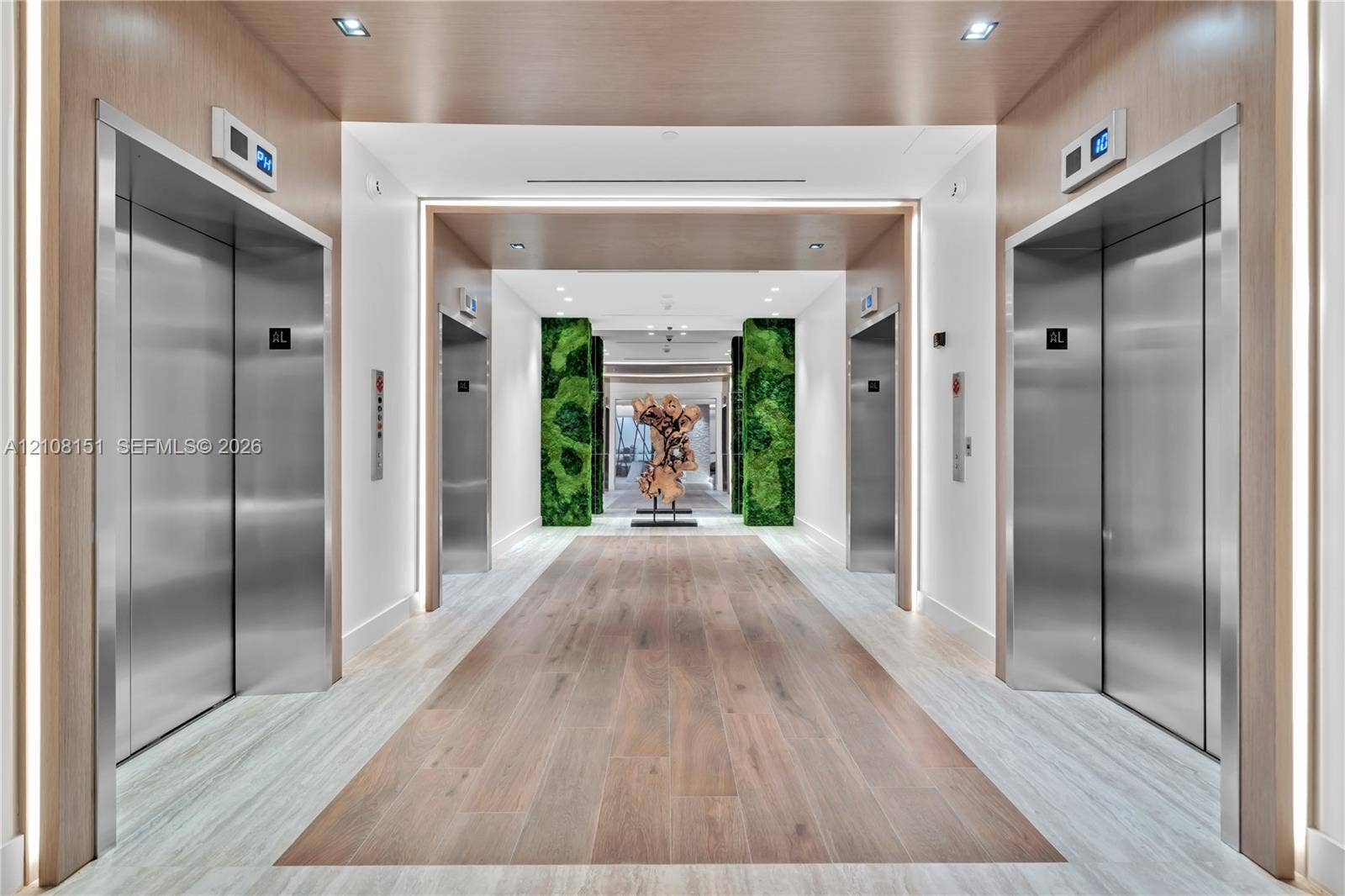 Elevator lobby featuring stainless steel doors, wood-finish wall paneling, integrated LED lighting, and decorative moss-covered columns