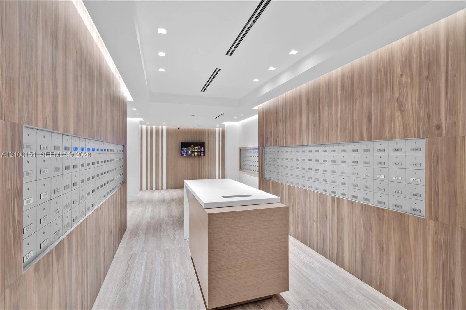 Modern lobby featuring wood-finish wall paneling, built-in parcel lockers, a central stone-topped island, recessed ceiling lighting, and wood-finish flooring