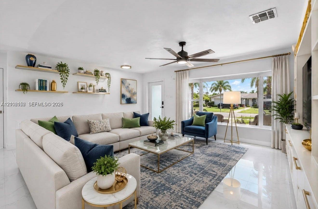 Living area featuring a large bay window, light-toned tile flooring, custom built-in cabinetry, floating wall shelves, and a ceiling fan