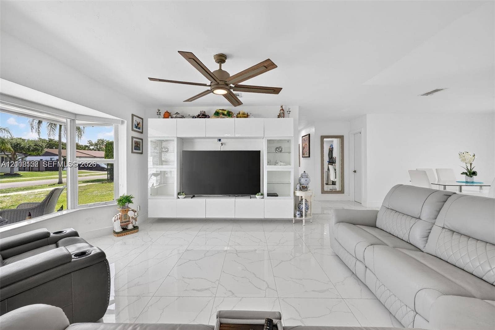 Living area featuring large-format tile flooring, a built-in white cabinetry unit with integrated shelving, and a six-blade ceiling fan