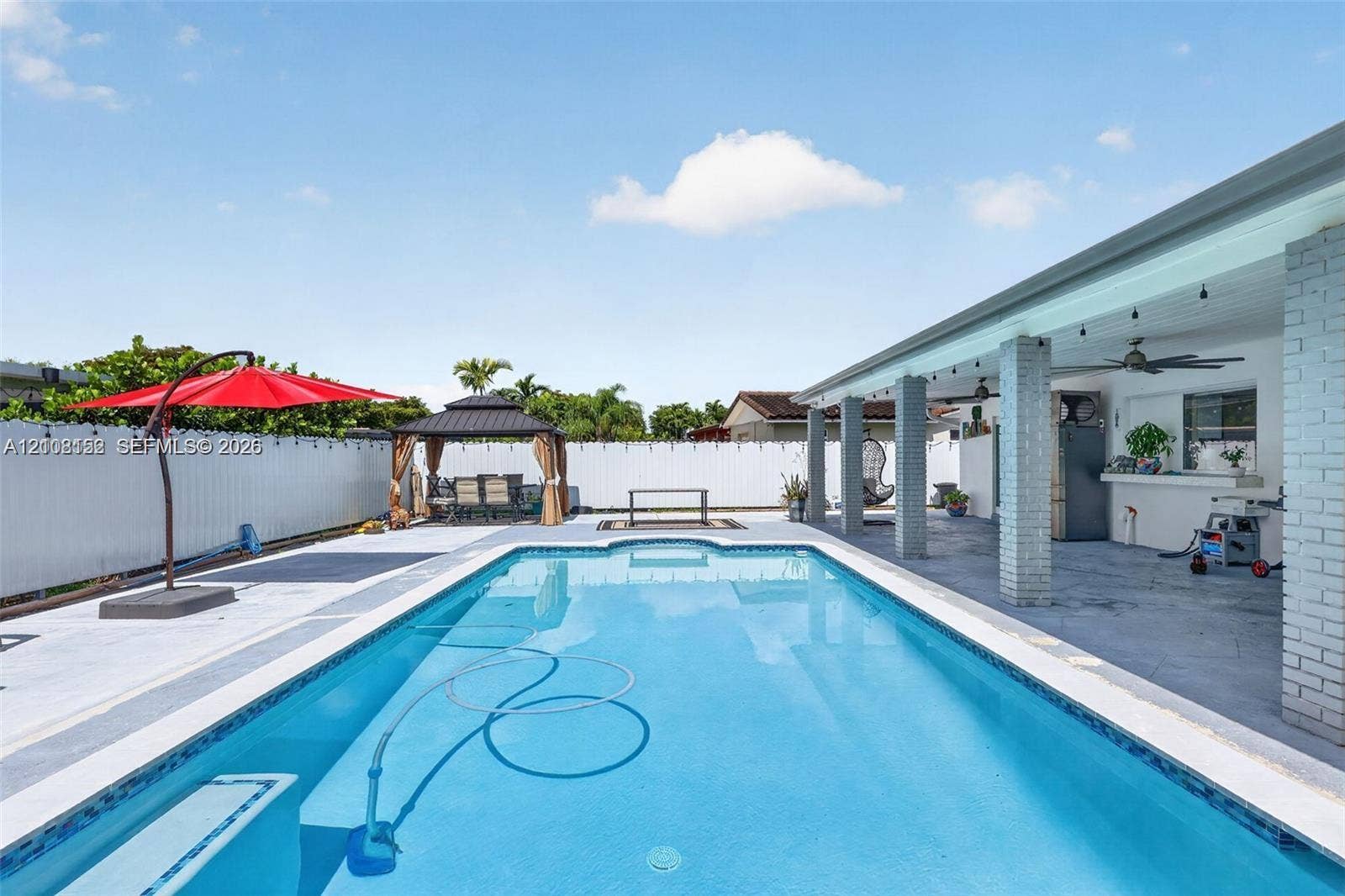 In-ground swimming pool with a tiled perimeter, expansive concrete patio, covered masonry lanai, and white vinyl privacy fencing