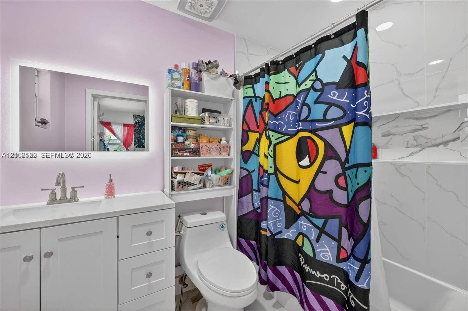 White vanity with integrated basin and polished chrome widespread faucet, LED-backlit mirror, and full-height shower surround featuring large-format stone-finish tiles