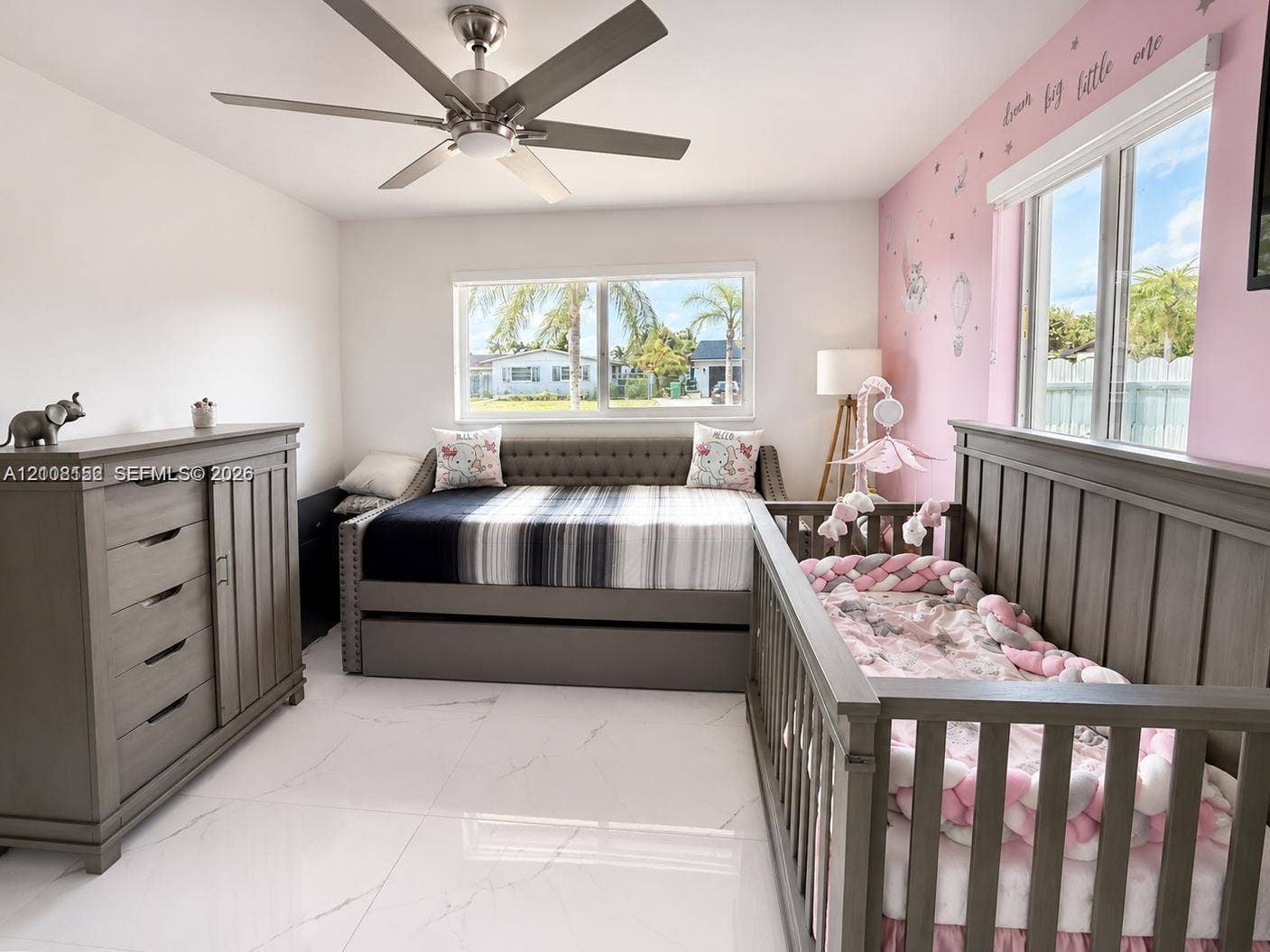 Bright room featuring large-format tile flooring, a brushed-nickel ceiling fan, and dual windows with natural light