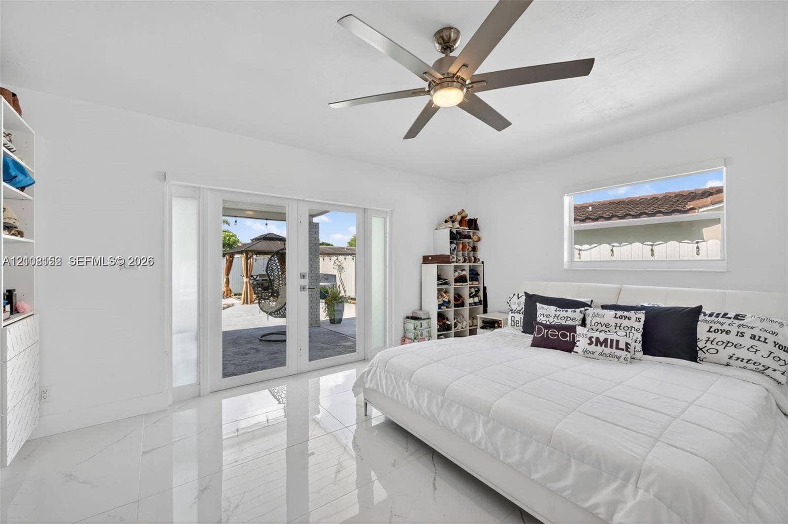 Glossy white tile flooring, ceiling fan with integrated lighting, built-in shelving, and dual glass-panel exterior doors