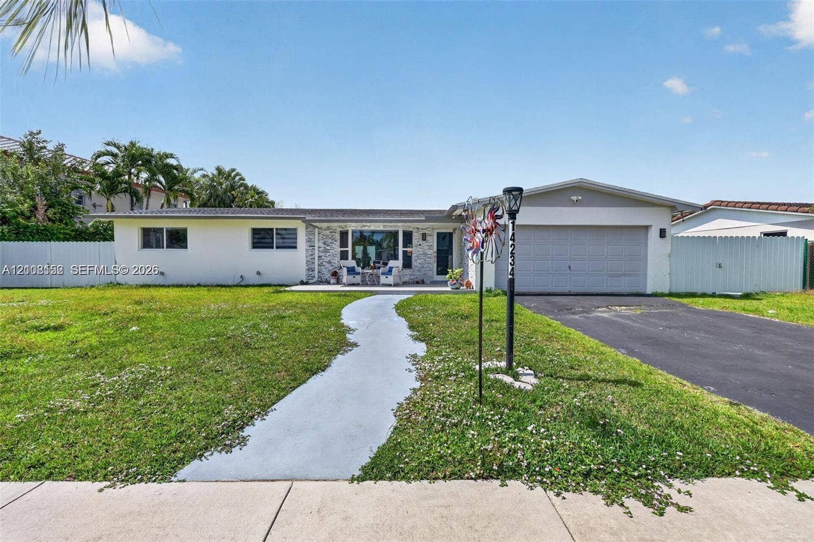 Single-story exterior featuring light-toned masonry accents, a paved front walkway, an attached two-car garage, and surrounding perimeter fencing