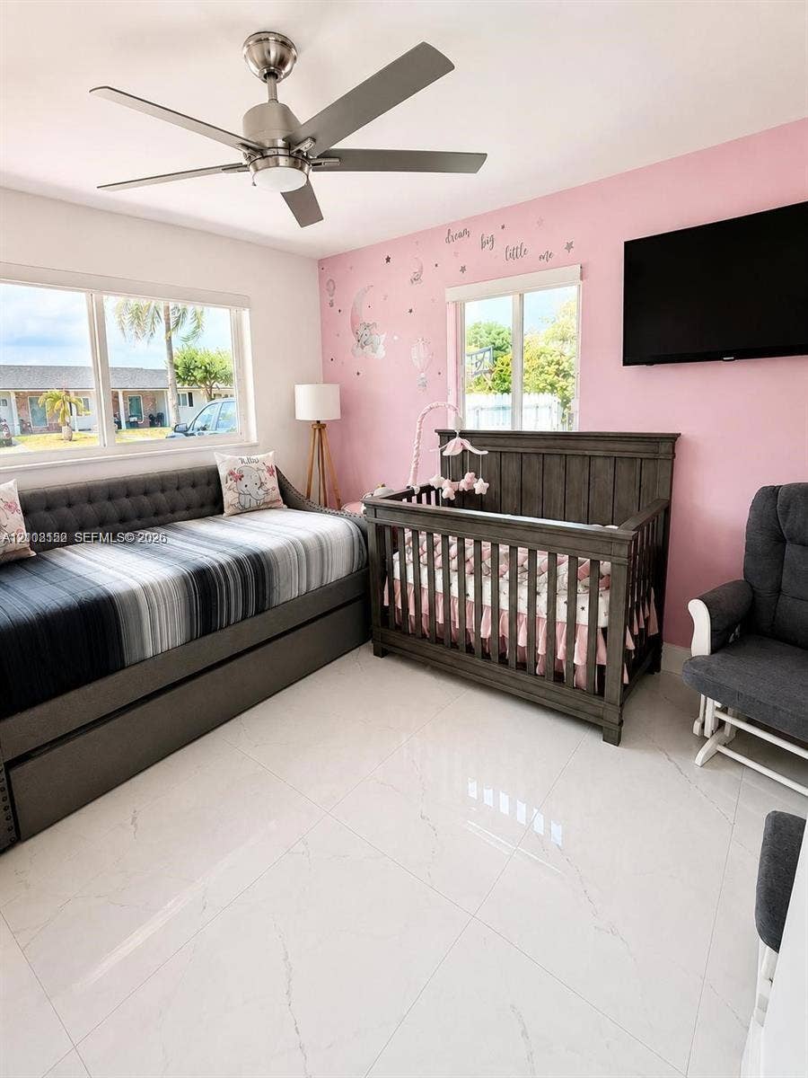 Room featuring large-format light-toned tile flooring, dual windows providing natural light, and a brushed nickel ceiling fan with integrated lighting