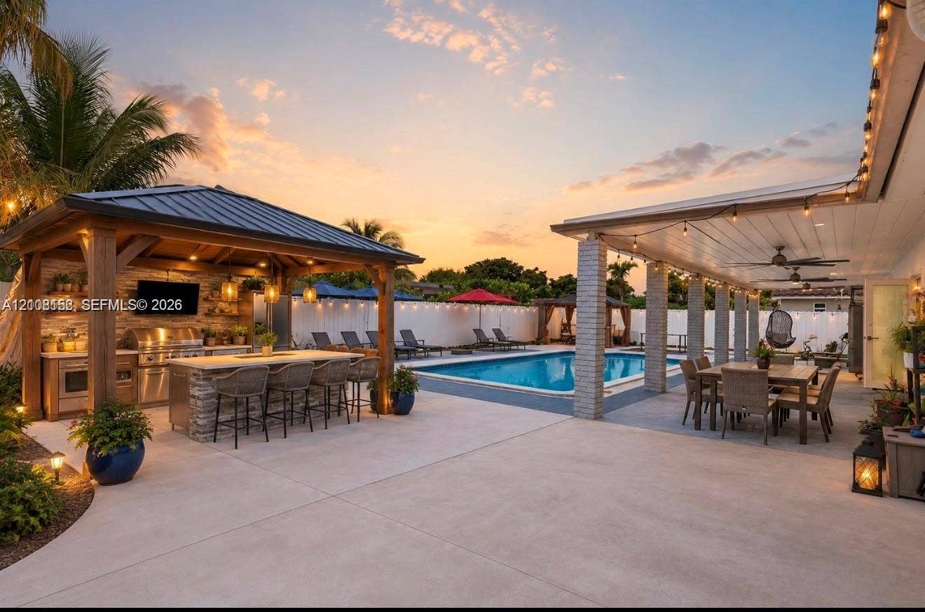 Outdoor living area featuring a covered patio, swimming pool, and a custom gazebo equipped with a built-in outdoor kitchen, stainless steel grill, and stone-finish island
