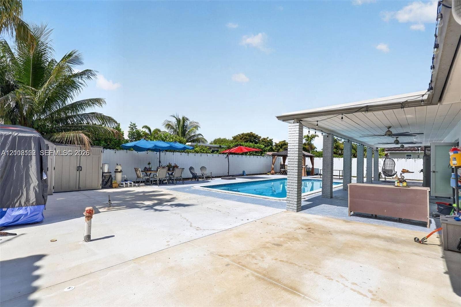 Outdoor living area featuring a covered patio with ceiling fans, an in-ground pool, expansive concrete hardscaping, and a white perimeter privacy fence