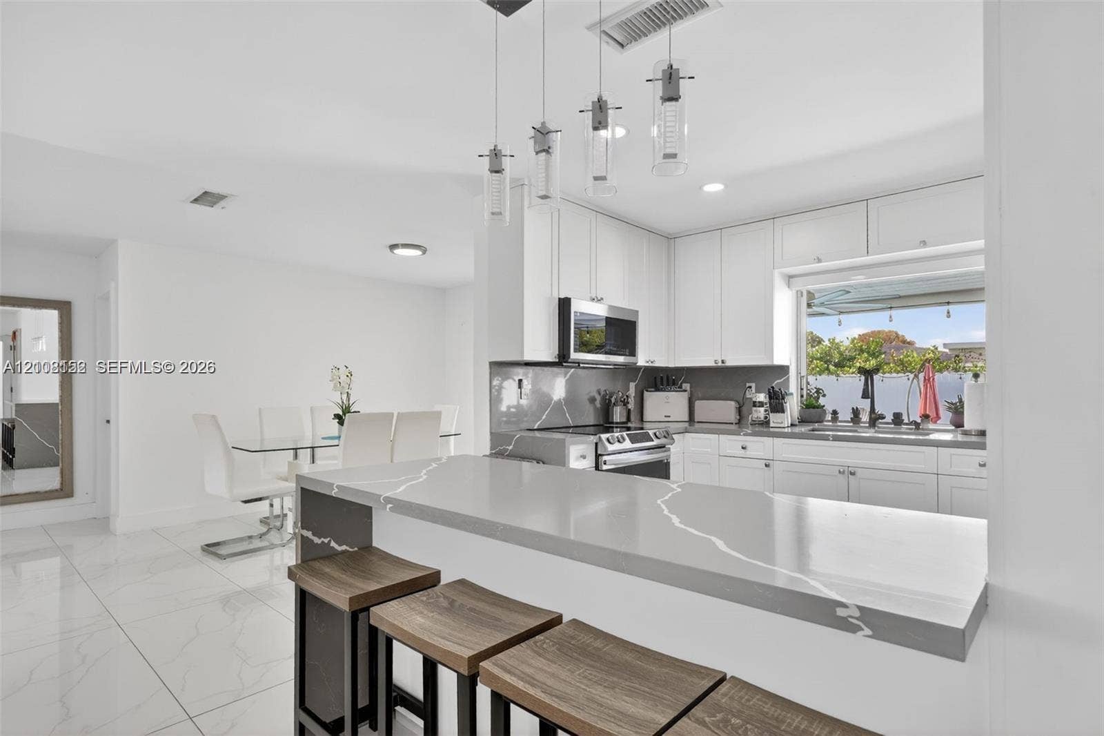 Kitchen featuring a waterfall-edge stone countertop, shaker-style cabinetry, stainless steel appliances, and multi-pendant lighting