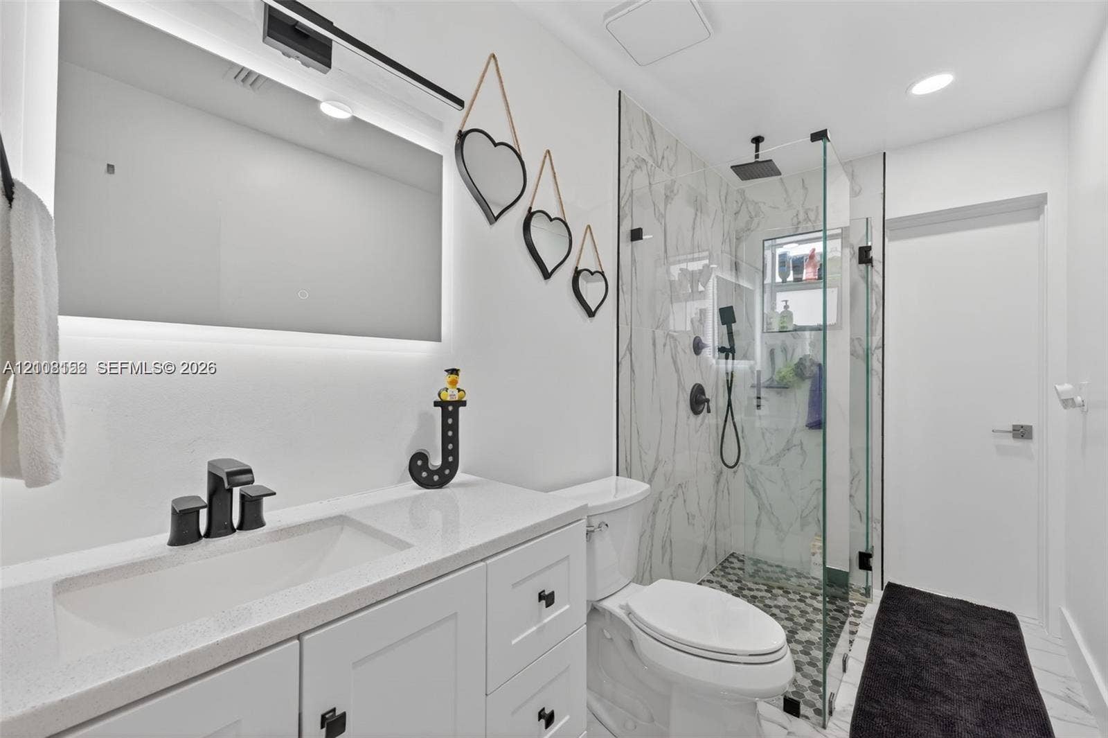 White cabinetry with quartz countertop, back-lit mirror, and matte black hardware