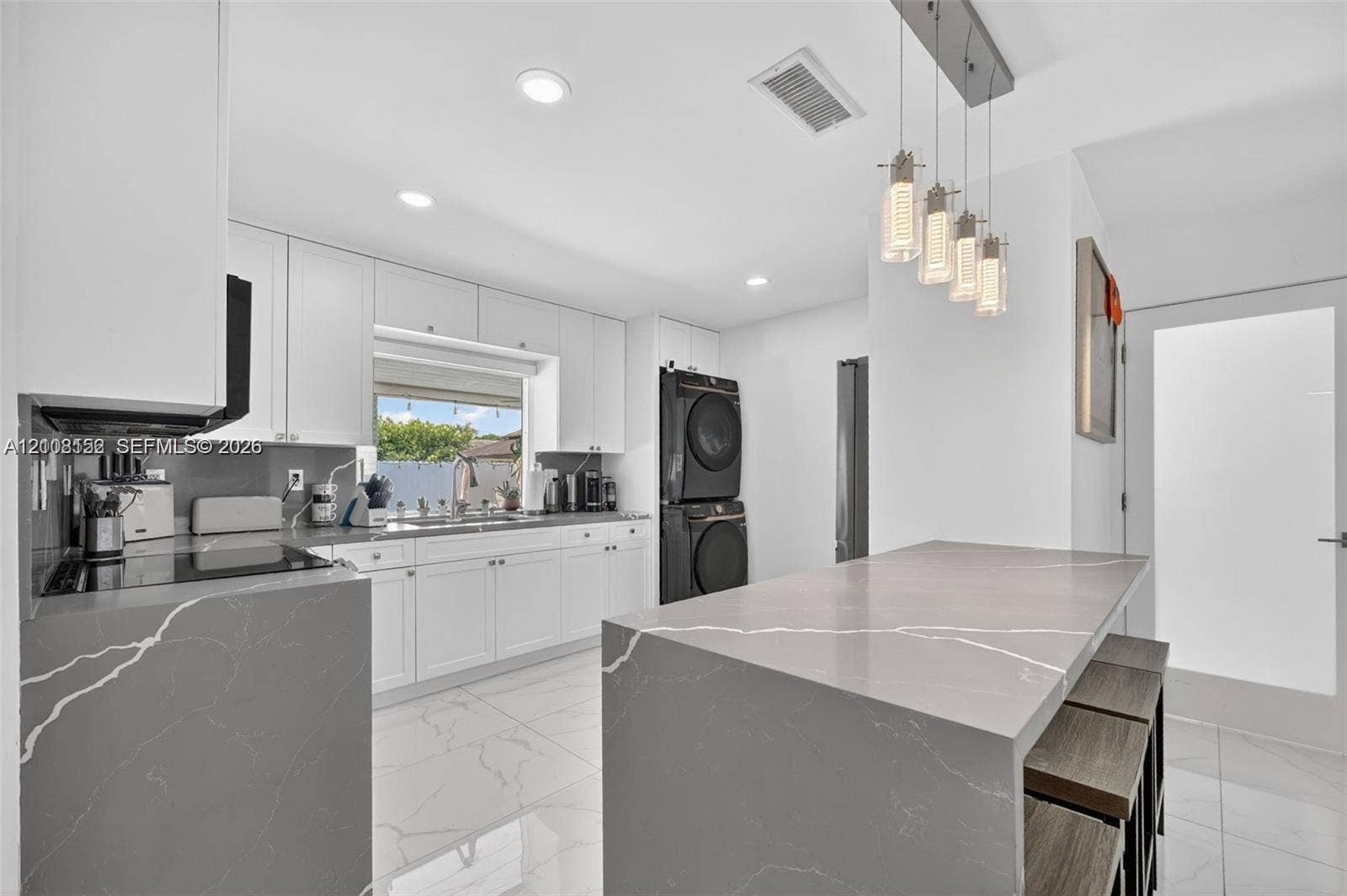 Kitchen featuring white cabinetry, grey stone-finish countertops with a waterfall edge, recessed lighting, multi-pendant fixture, and white tile flooring