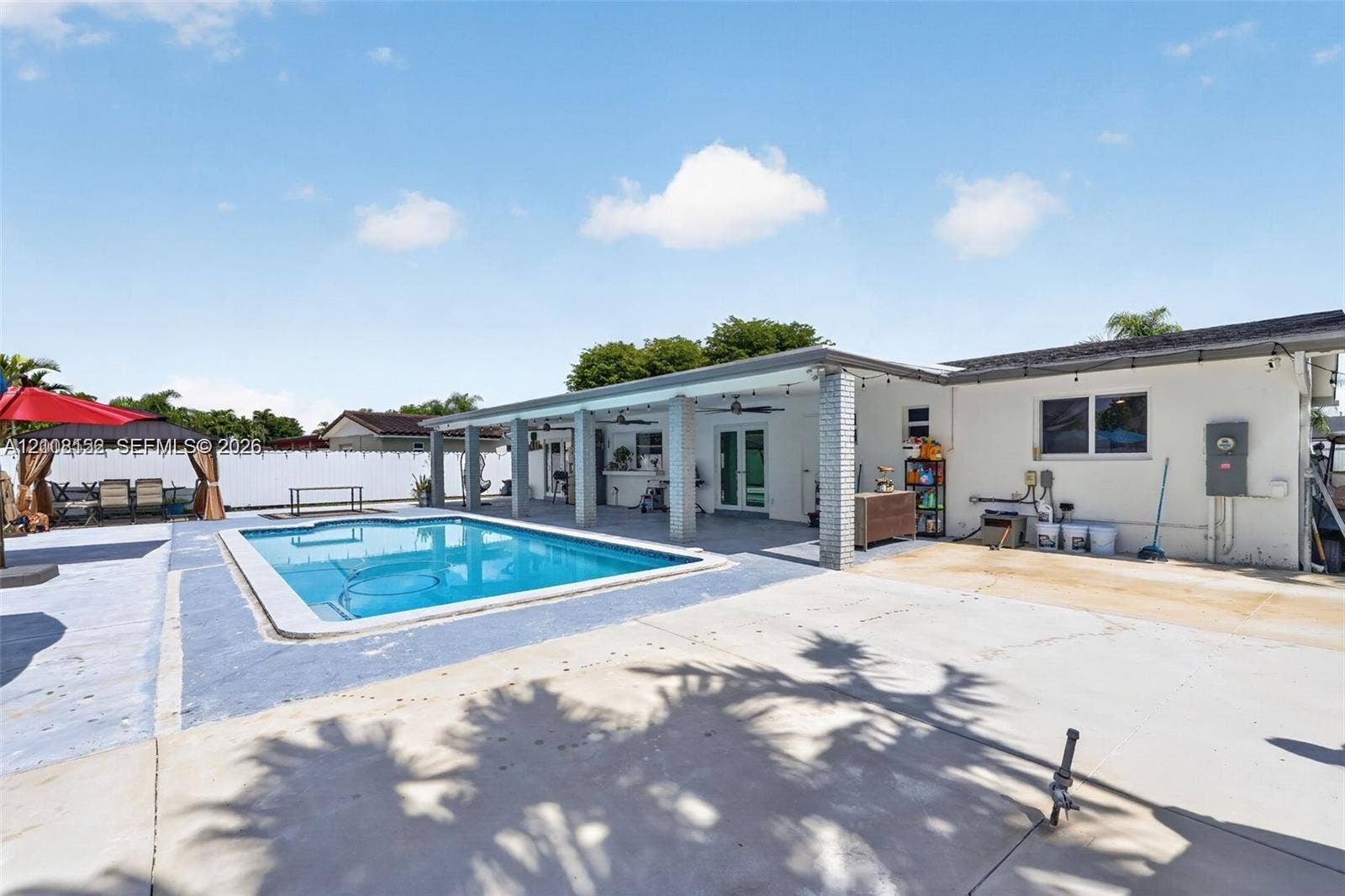 Backyard featuring an inground swimming pool, concrete patio, and a covered lanai with brick support columns