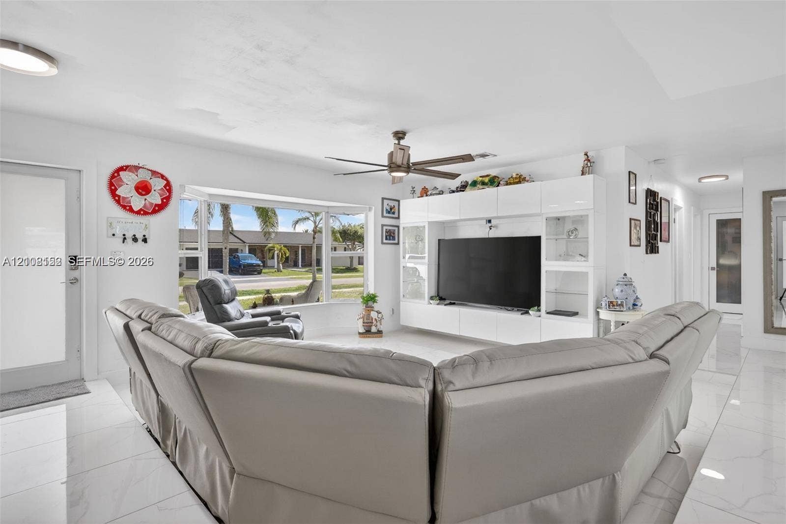Living area featuring large-format tile flooring, a bay window, and a built-in media console with glossy white cabinetry and integrated display shelving