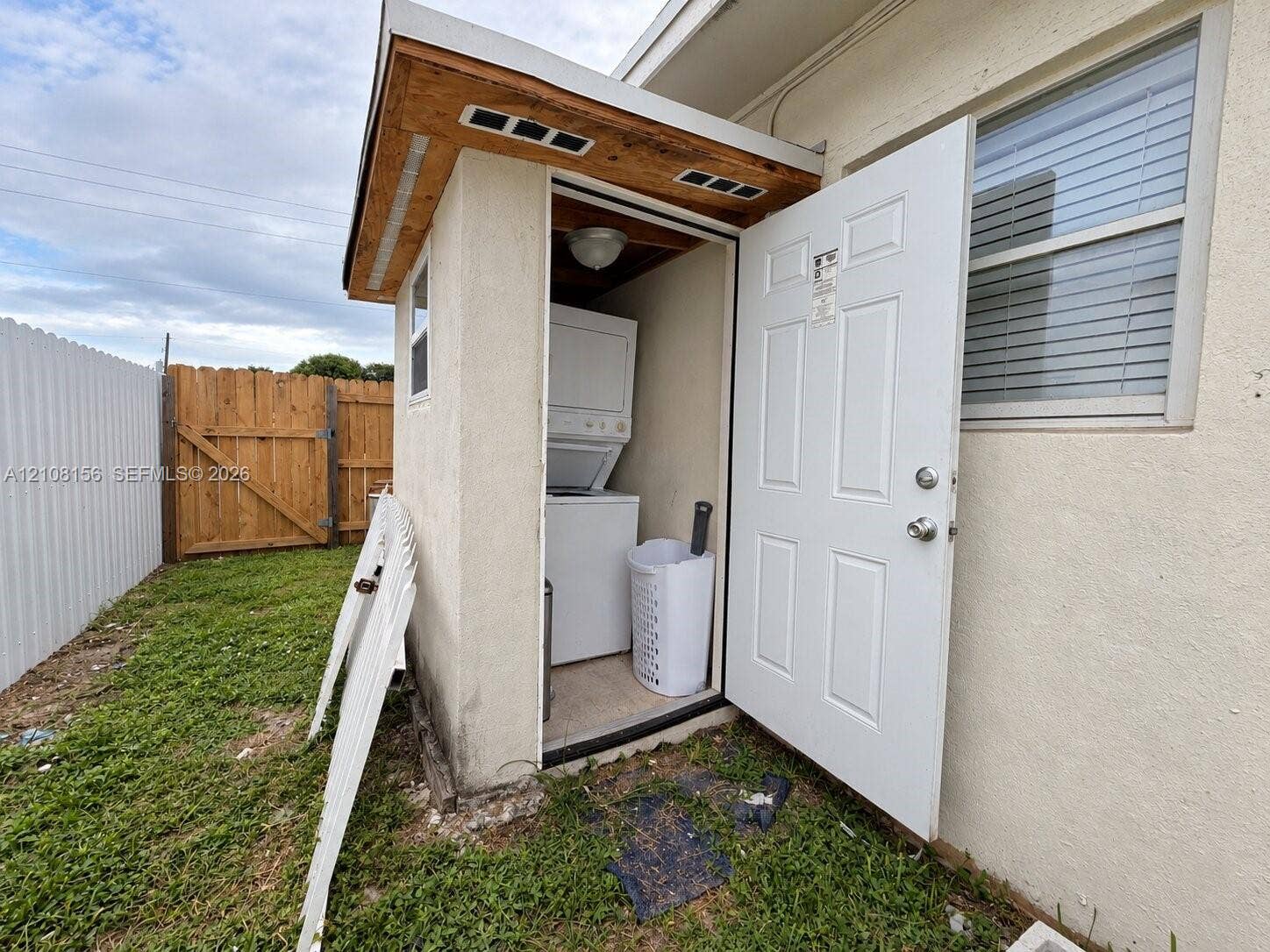 17175 NW 41st Avenue, Miami Gardens, FL 33055 Exterior utility enclosure featuring a stucco finish, a shingled shed-style roof, a single-entry door, and stacked laundry appliances