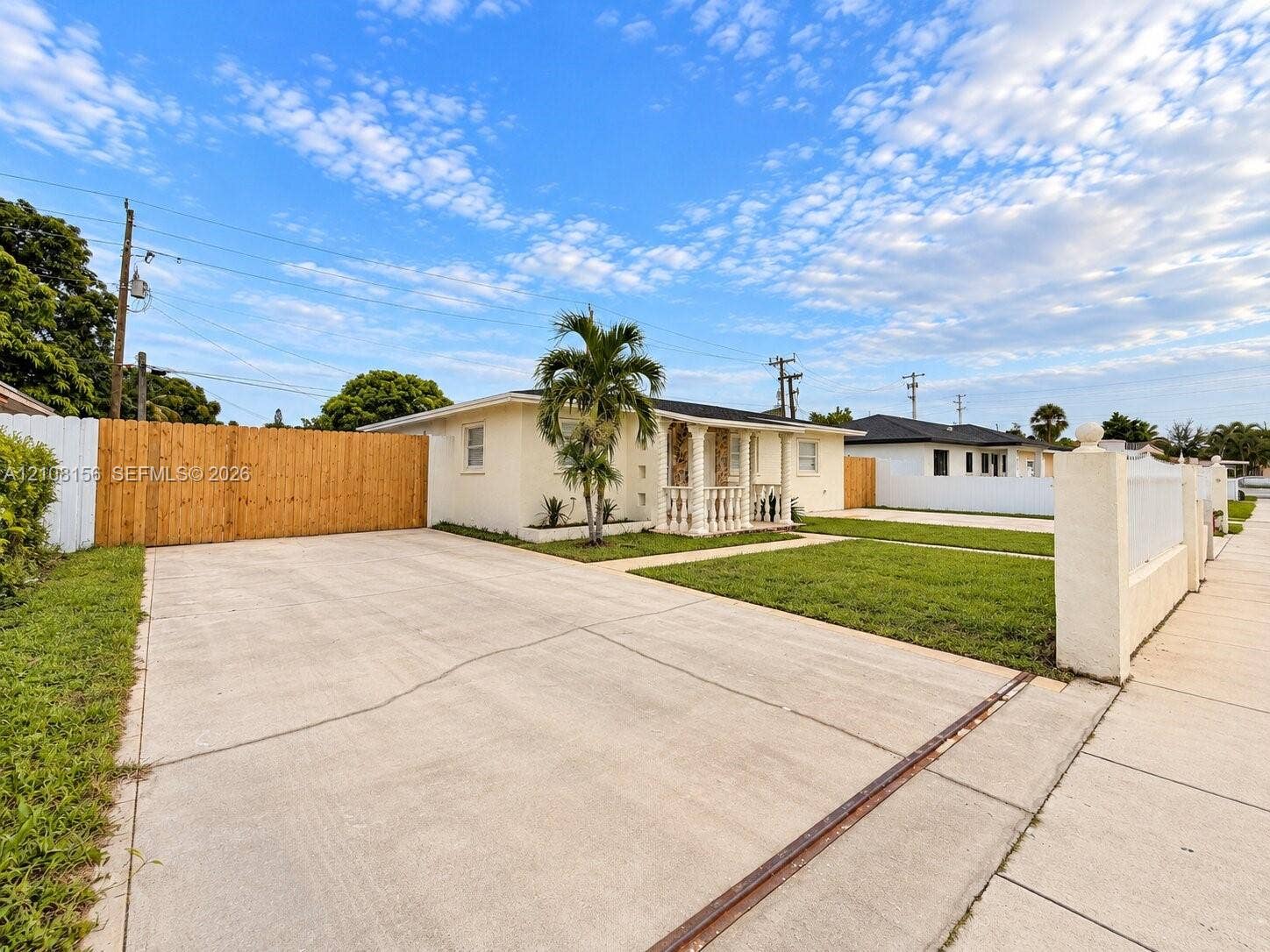 17175 NW 41st Avenue, Miami Gardens, FL 33055 Single-story exterior featuring a concrete driveway, gated wooden fence, front covered porch with decorative columns, and manicured lawn
