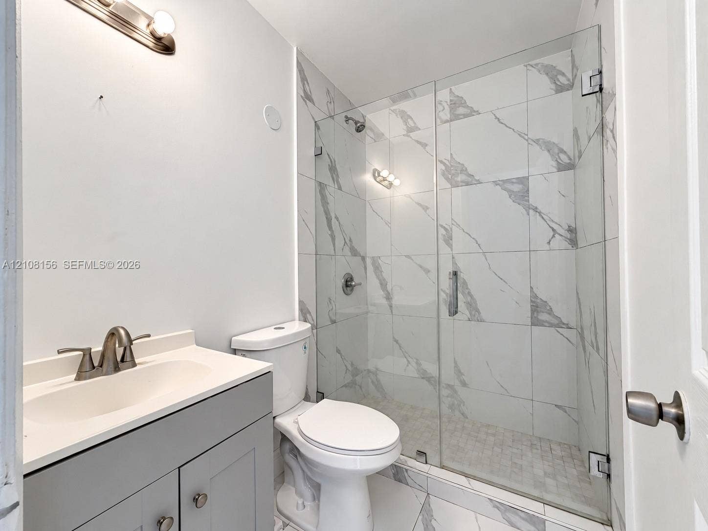 17175 NW 41st Avenue, Miami Gardens, FL 33055 Bathroom featuring a grey shaker-style vanity with an integrated sink, walk-in shower with large-format stone-patterned tile, frameless glass enclosure, and modern brushed-metal fixtures