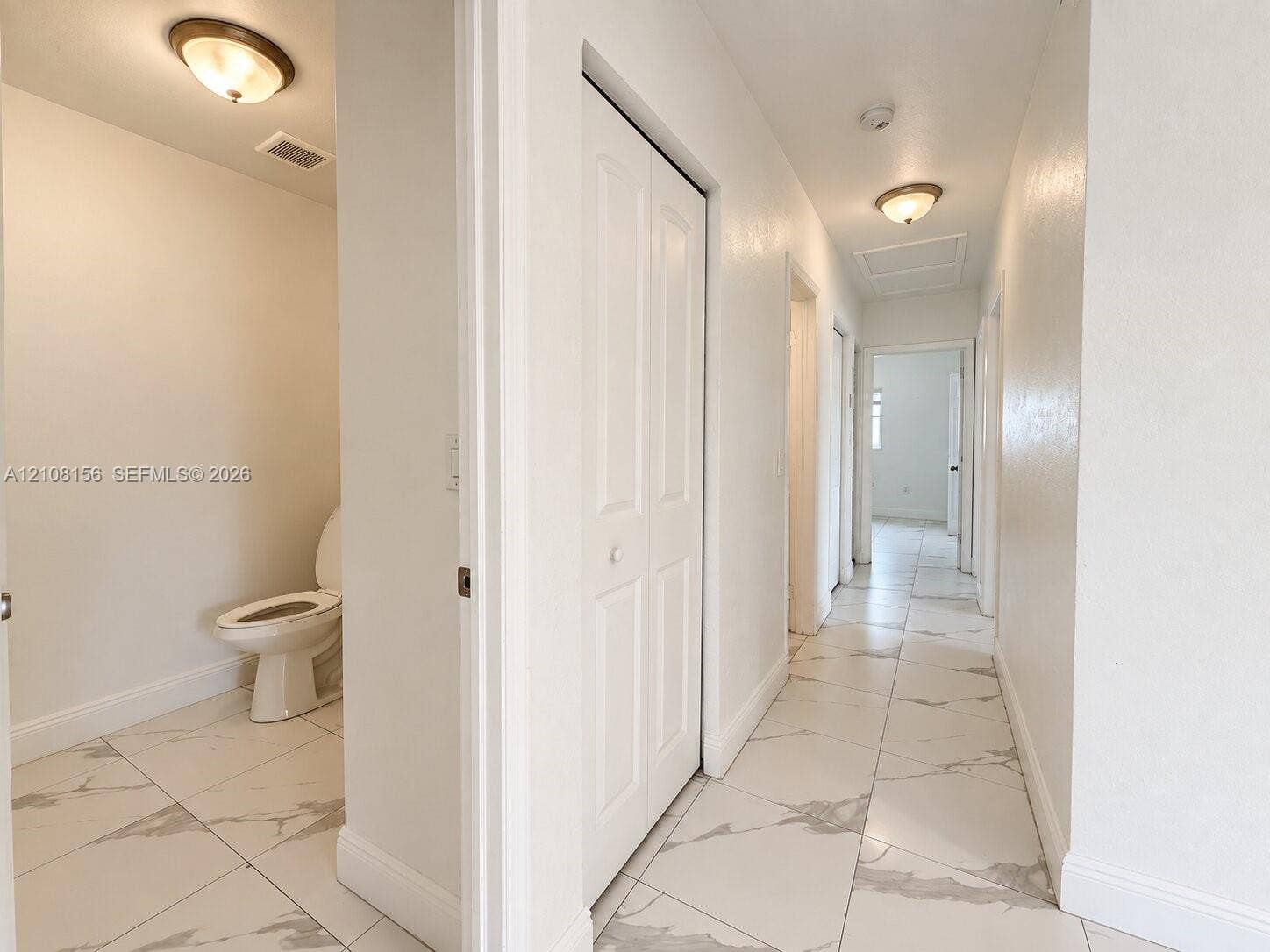 17175 NW 41st Avenue, Miami Gardens, FL 33055 Hallway featuring large-format white stone-finish floor tiles with grey veining, crisp neutral wall paint, white bi-fold closet doors, and flush-mount lighting fixtures