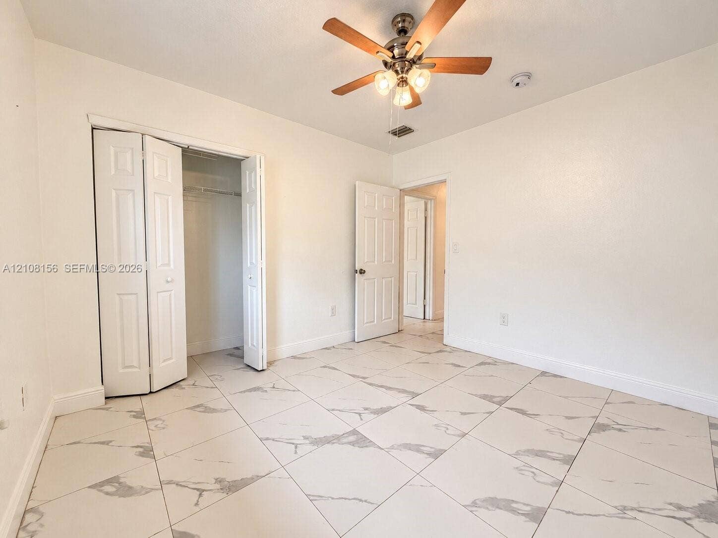 17175 NW 41st Avenue, Miami Gardens, FL 33055 Neutral-toned interior featuring large-format tile flooring with a marble-finish pattern, a ceiling-mounted light fixture with a fan, and bi-fold closet doors