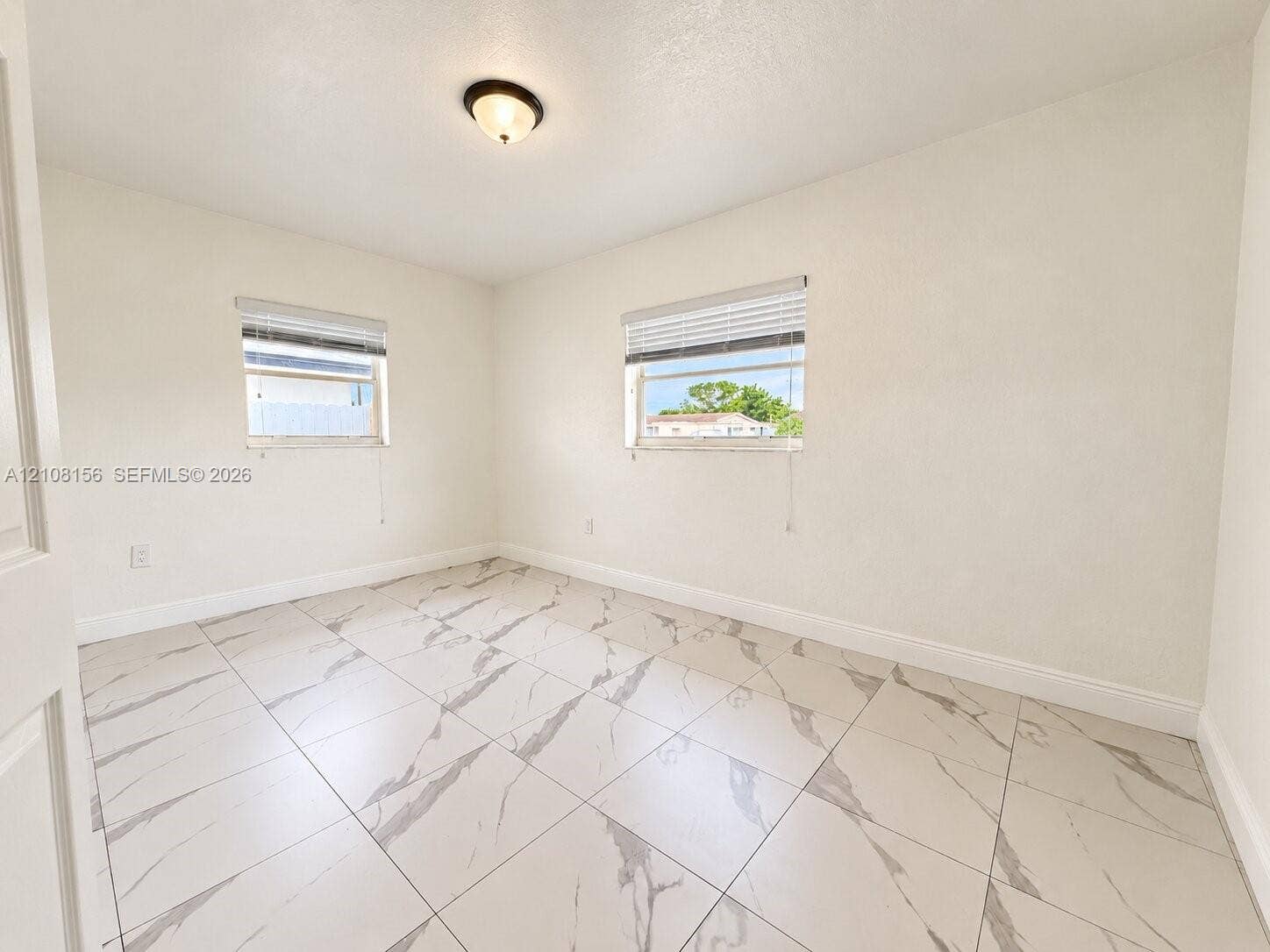 17175 NW 41st Avenue, Miami Gardens, FL 33055 Room featuring large-format tile flooring with veining, two windows with horizontal blinds, and a centered flush-mount light fixture