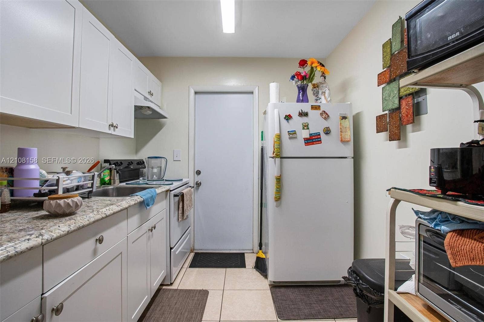 Kitchen featuring white cabinetry, stone-finish countertops, stainless steel sink, and tile flooring