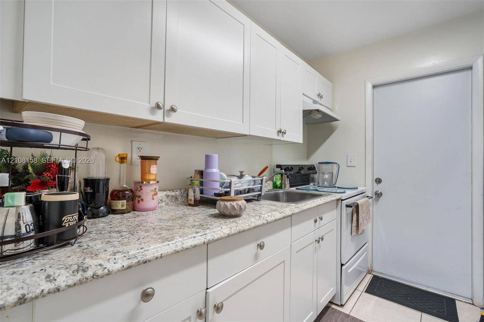 Kitchen featuring white shaker-style cabinetry, speckled stone-finish countertops, stainless steel sink, and tile flooring