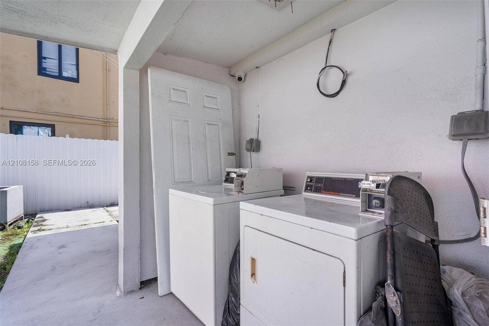 Covered concrete utility area featuring painted masonry walls and coin-operated laundry equipment
