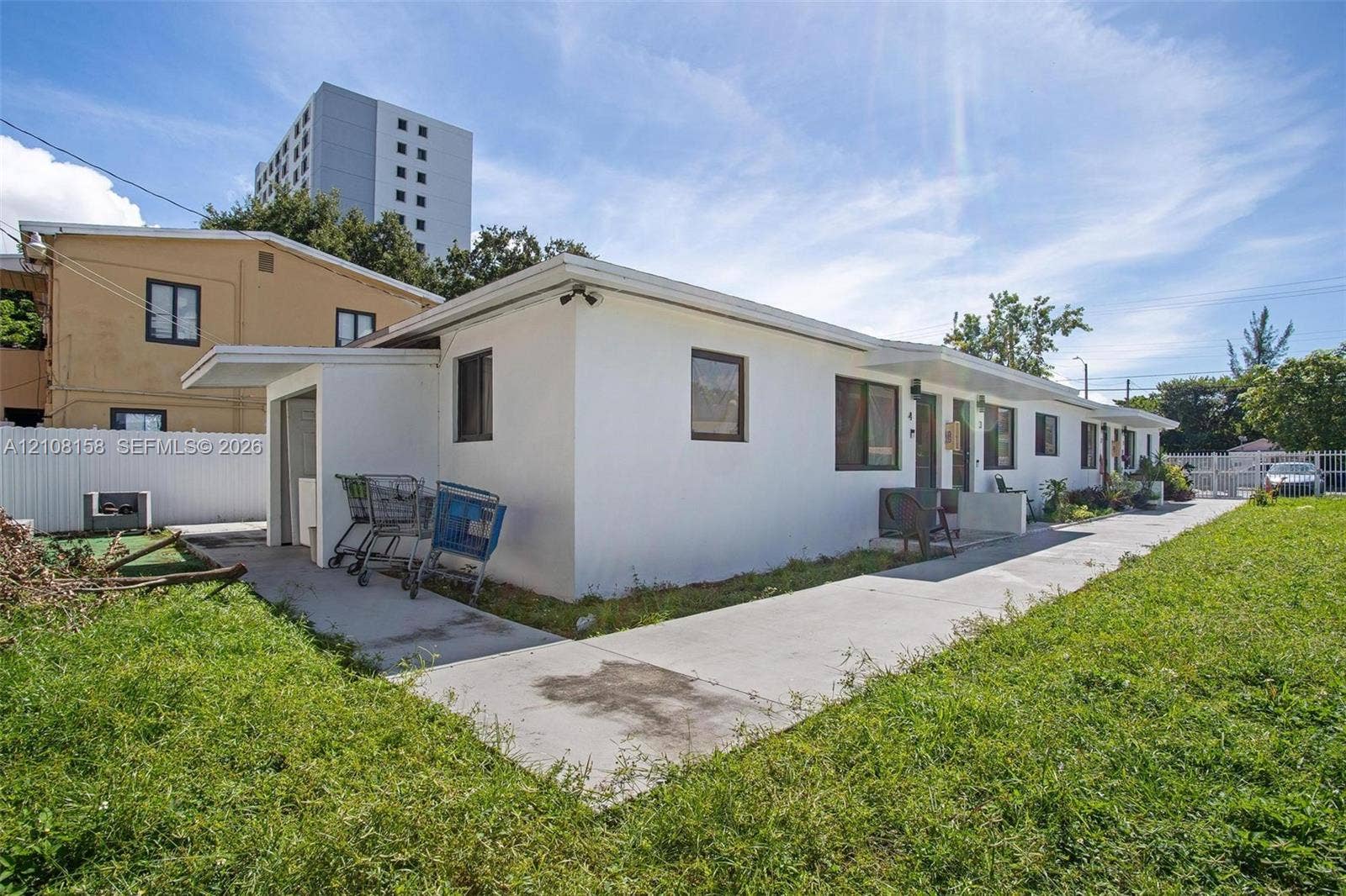 Single-story exterior featuring a white stucco facade, flat roofline, dark-trimmed windows, and an expansive concrete walkway