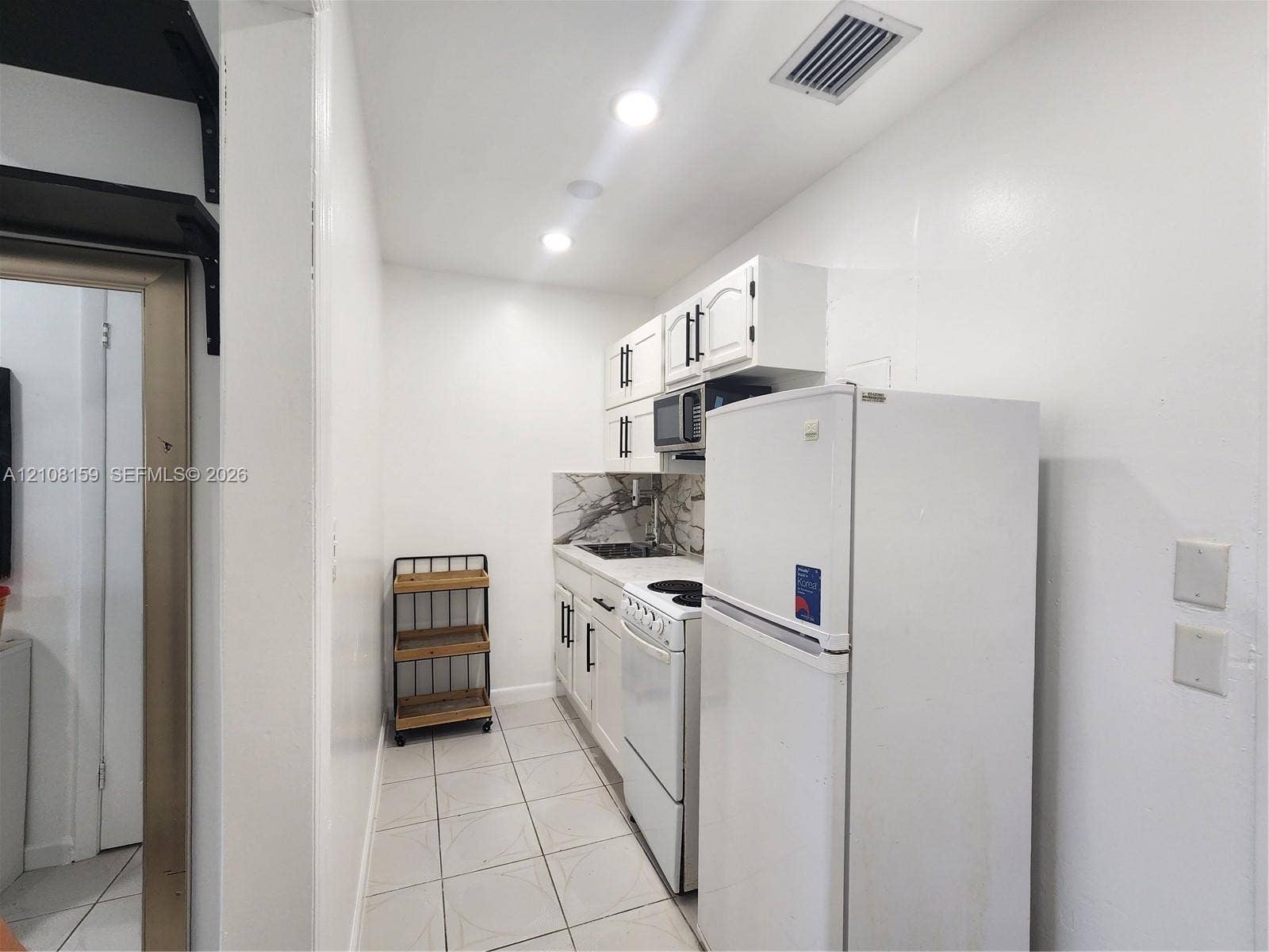 Kitchen featuring white cabinetry with dark hardware, patterned stone-finish backsplash, recessed lighting, and tile flooring