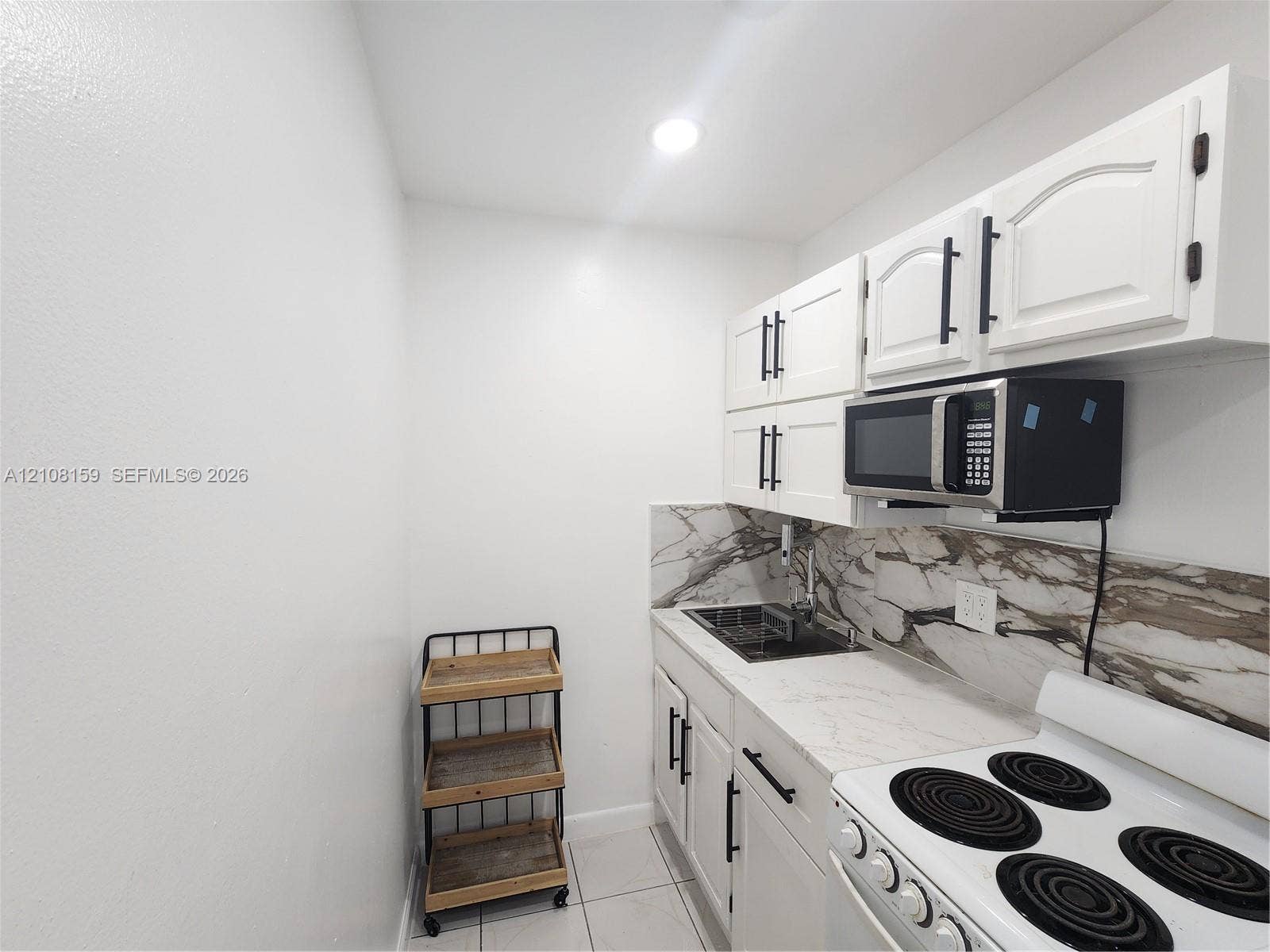 Kitchen featuring white cabinetry with matte black hardware, stone-patterned backsplash, light-toned countertop, integrated sink, and white electric range