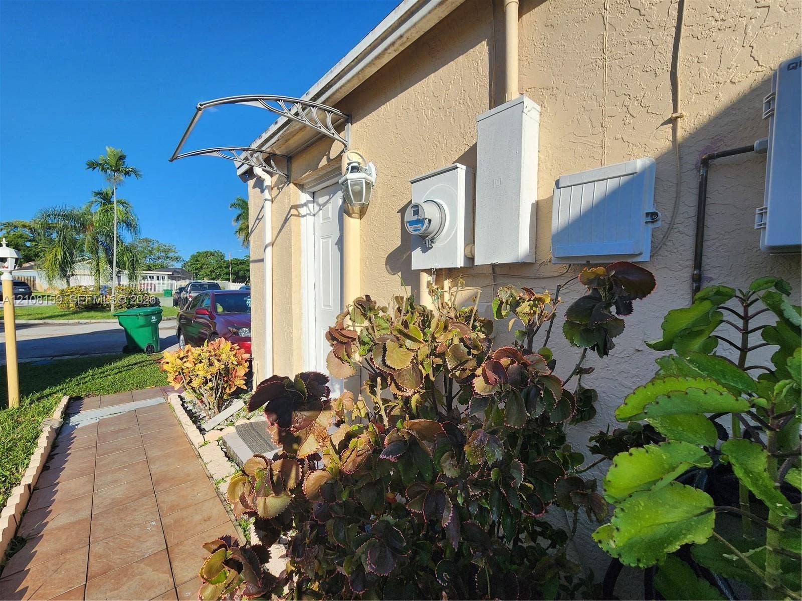 Stucco exterior featuring a tiled walkway, metal door awning, and wall-mounted exterior lighting