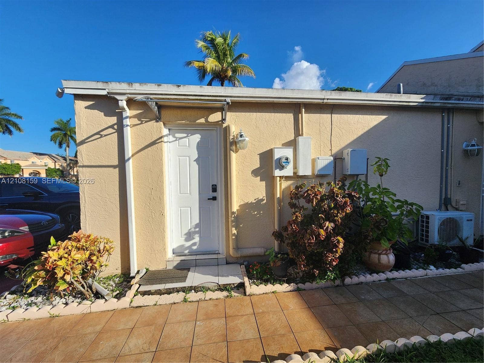 Stucco exterior featuring a white paneled entry door, tiled walkway, and mounted outdoor lighting fixtures