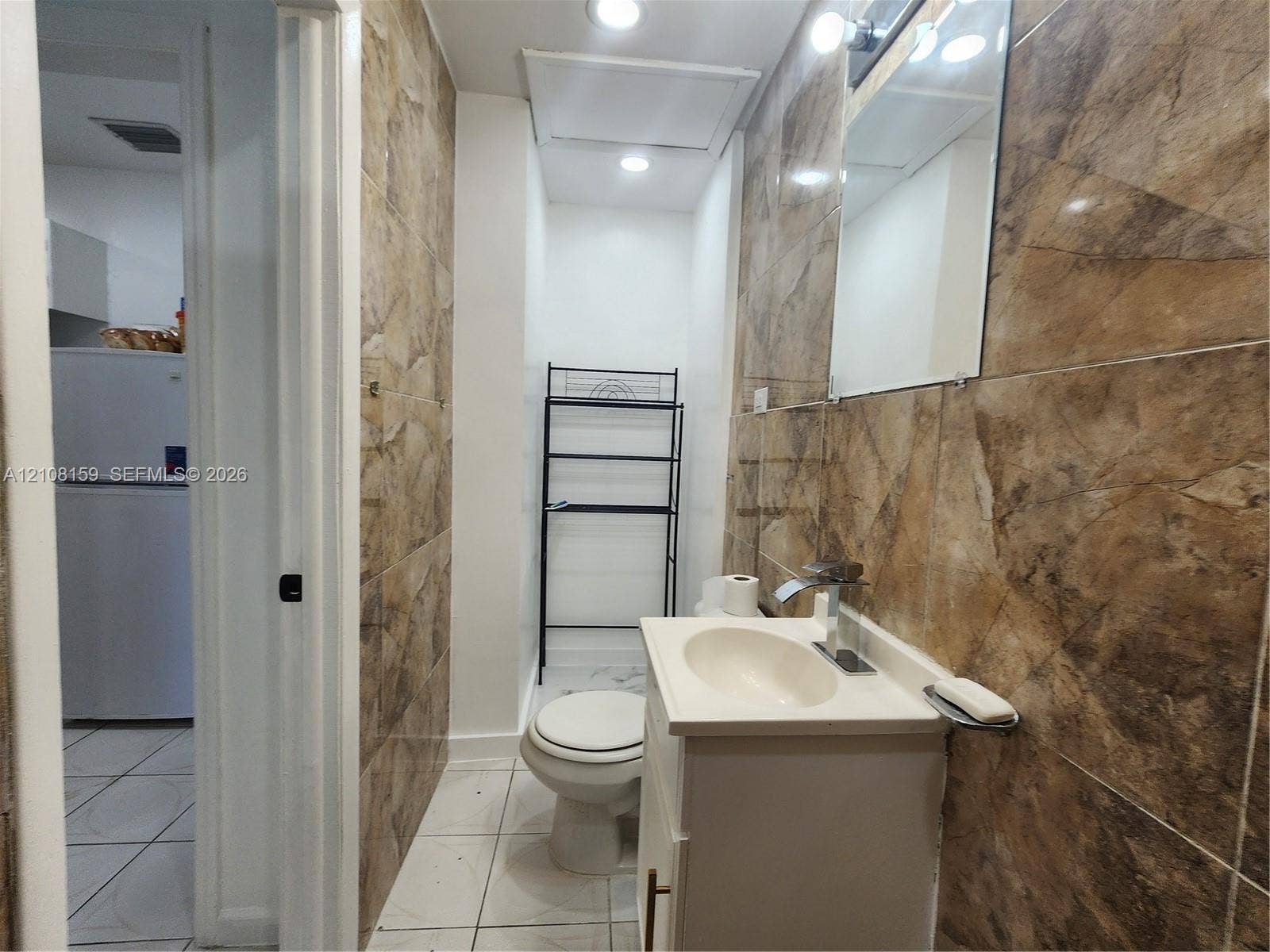Bathroom featuring floor-to-ceiling large-format tile walls, white tile flooring, a built-in vanity with a sink, and a wall-mounted mirror