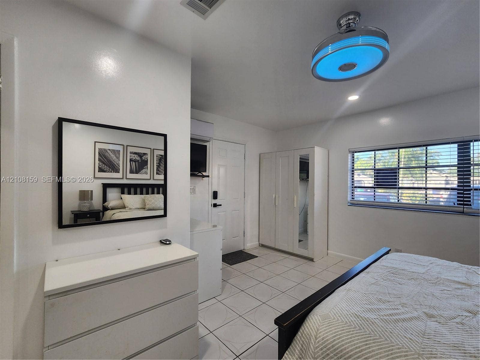 Ceramic tile flooring, minimalist ceiling fan with integrated lighting, wall-mounted mini-split system, and horizontal window blinds