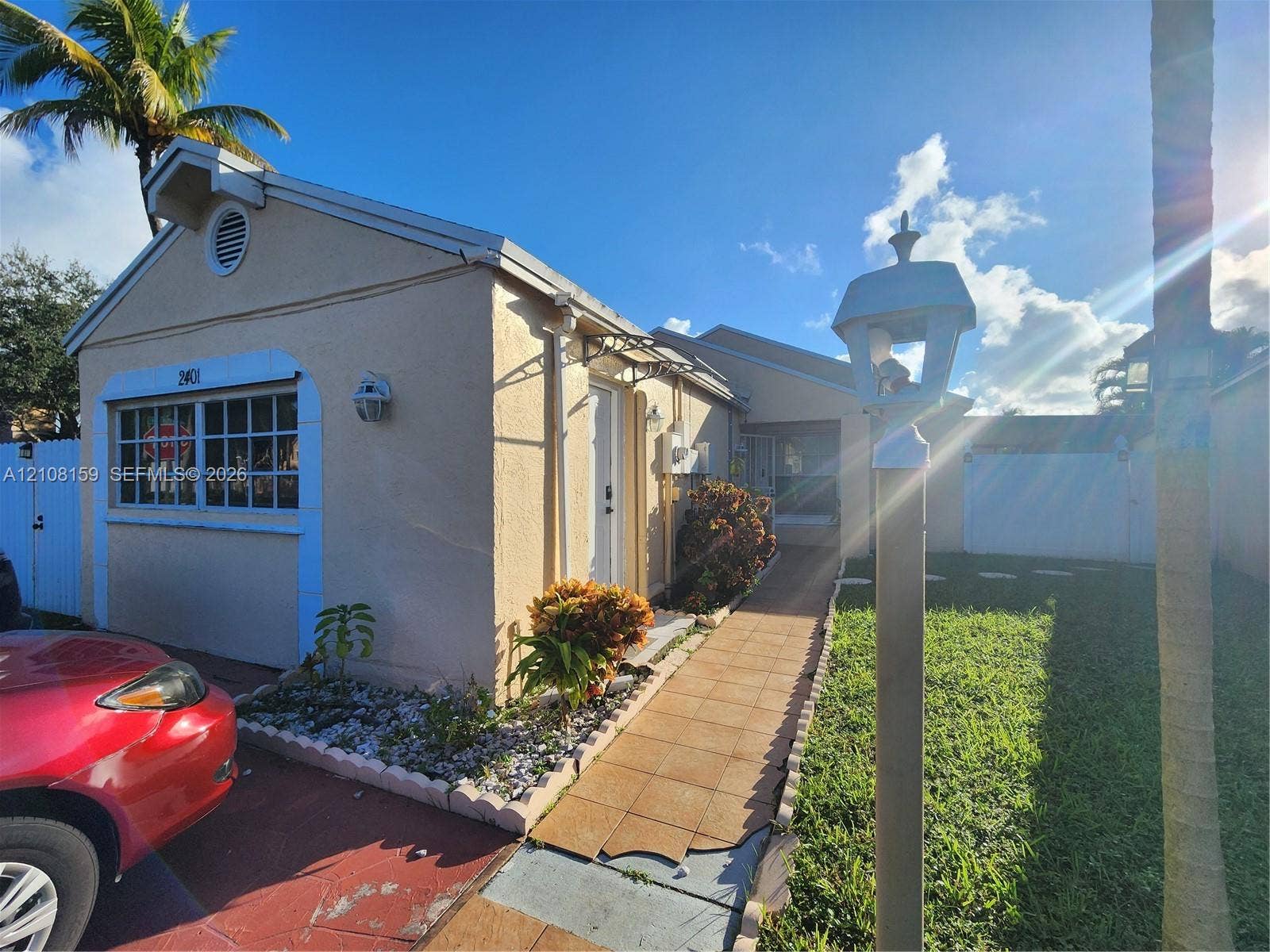 Stucco exterior residence featuring a tiled walkway, manicured lawn, scalloped landscape edging, and exterior lamppost