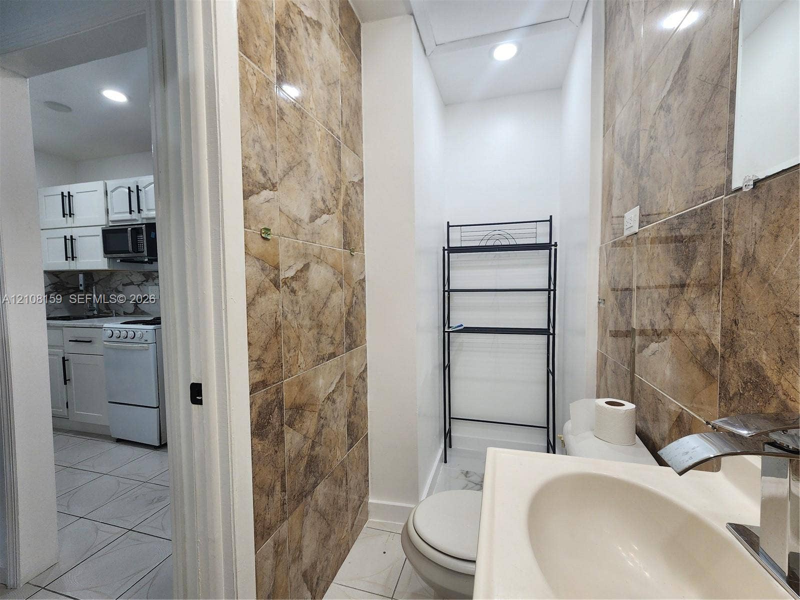 Bathroom featuring floor-to-ceiling tile surrounds, a pedestal sink with a modern faucet, and recessed lighting