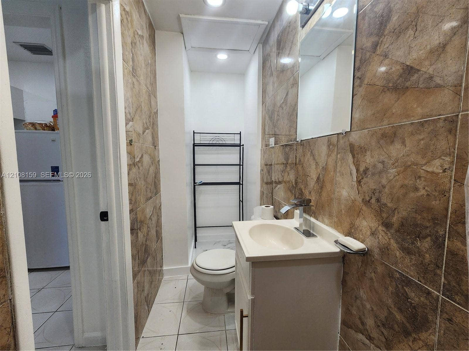 Bathroom featuring floor-to-ceiling stone-patterned wall tile, white vanity cabinet with integrated sink, chrome faucet, and recessed lighting