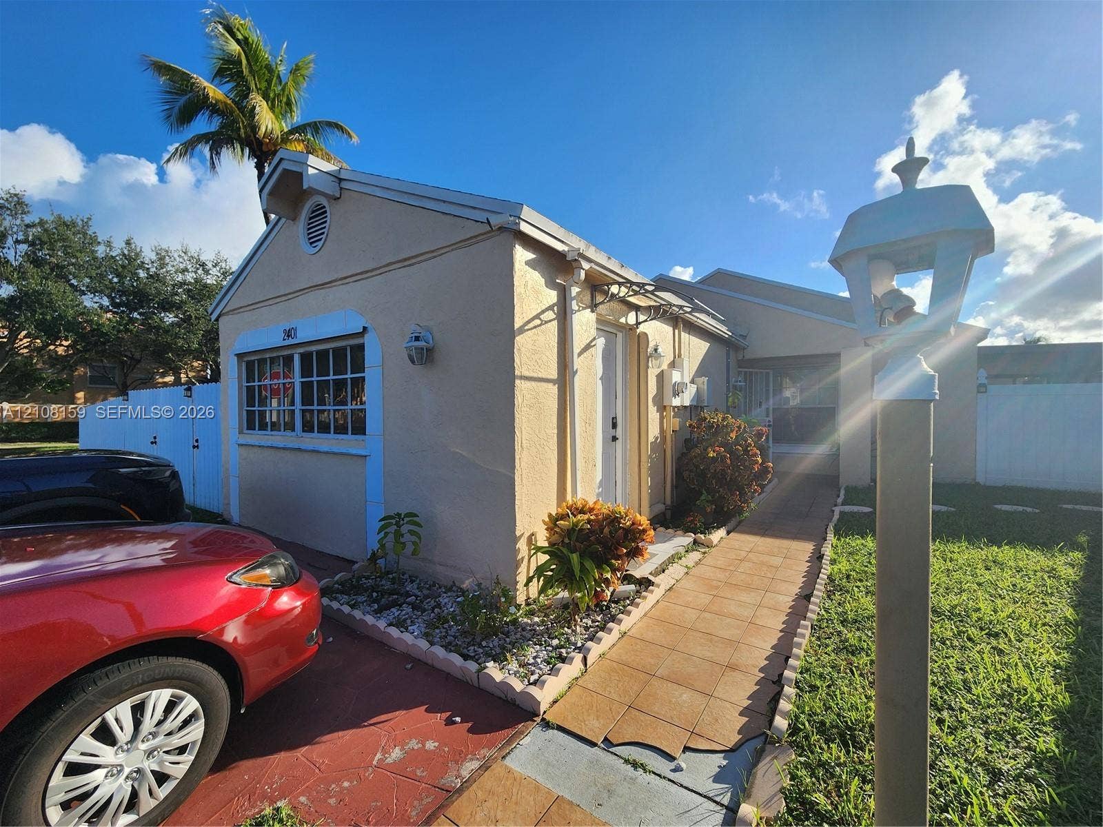 Stucco exterior featuring decorative trim, a grid-pattern window, tiled entryway walkway, and a decorative post lamp
