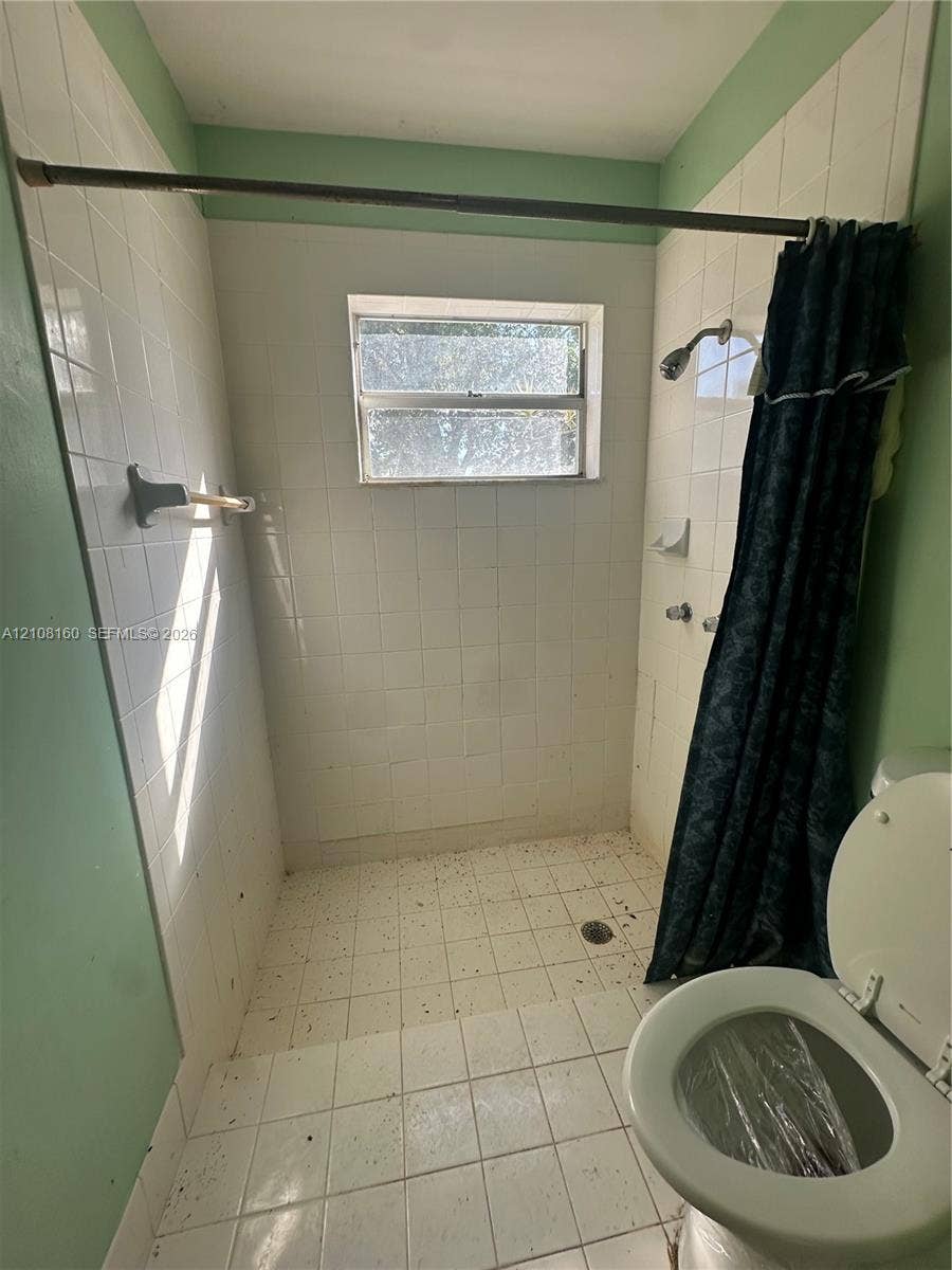 1262 NW 126th Avenue, Sunrise, FL 33323 Walk-in shower enclosure featuring white square tile surround, integrated soap dish, chrome shower head, and central window