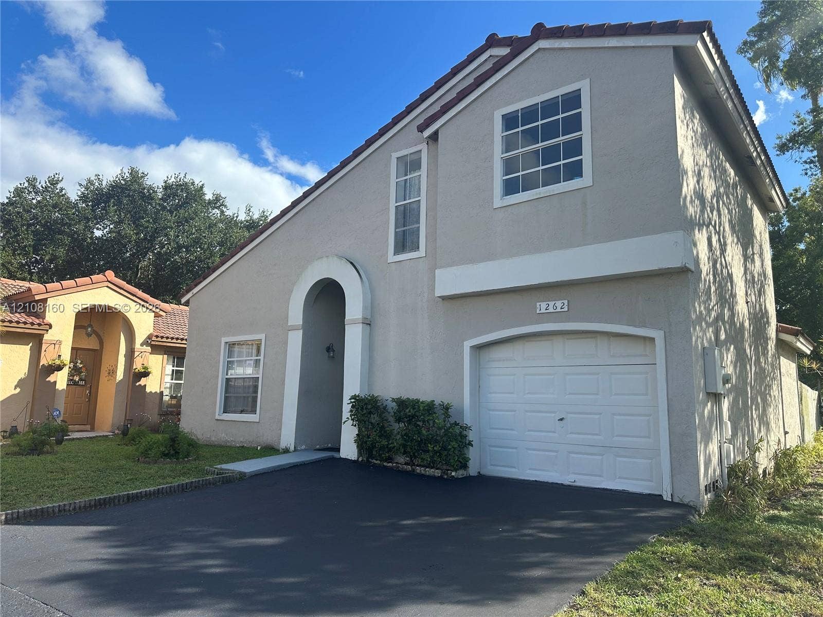 1262 NW 126th Avenue, Sunrise, FL 33323 Two-story exterior featuring a stucco facade, tiled roof, arched entryway, and an attached single-car garage with a paved driveway