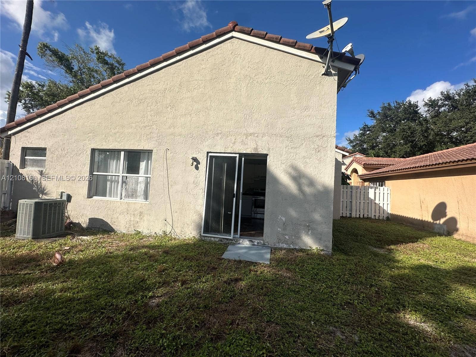 1262 NW 126th Avenue, Sunrise, FL 33323 Stucco exterior featuring a tiled roof, sliding glass doors, and a private yard with white vinyl fencing