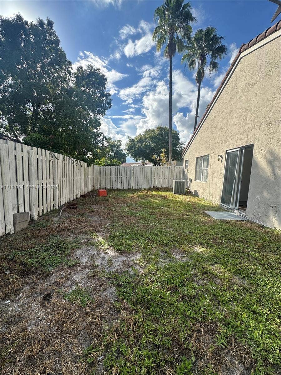 1262 NW 126th Avenue, Sunrise, FL 33323 Private backyard featuring a stucco exterior, vertical panel fencing, and mature palm trees