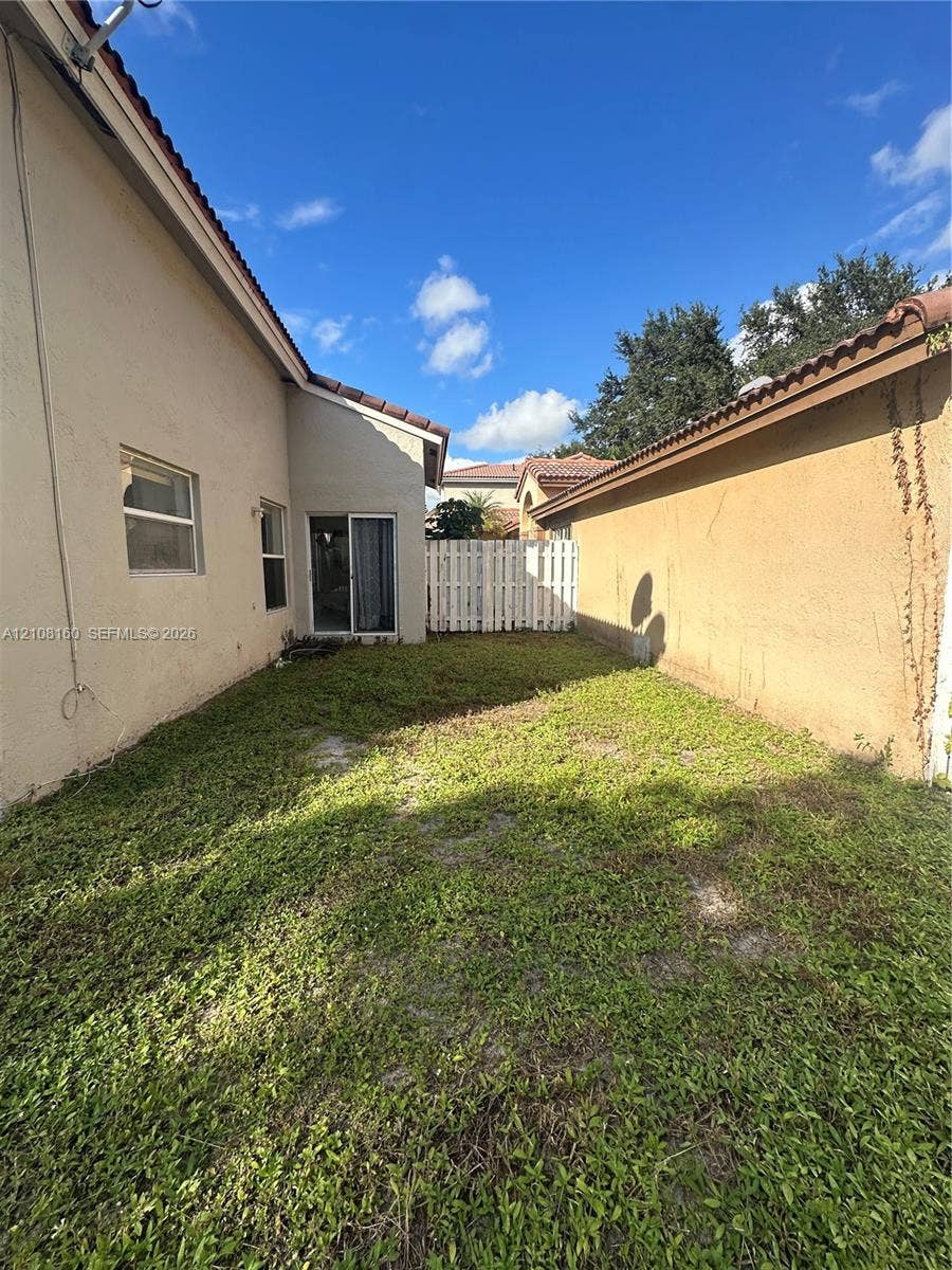 1262 NW 126th Avenue, Sunrise, FL 33323 Side yard exterior featuring stucco siding, tile roofline, sliding glass door, and a white privacy fence
