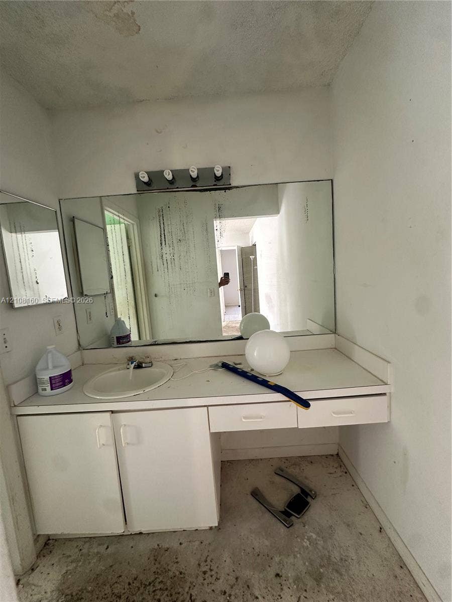 1262 NW 126th Avenue, Sunrise, FL 33323 Built-in vanity featuring white cabinetry, integrated sink, and an expansive wall-mounted mirror with a multi-bulb light fixture