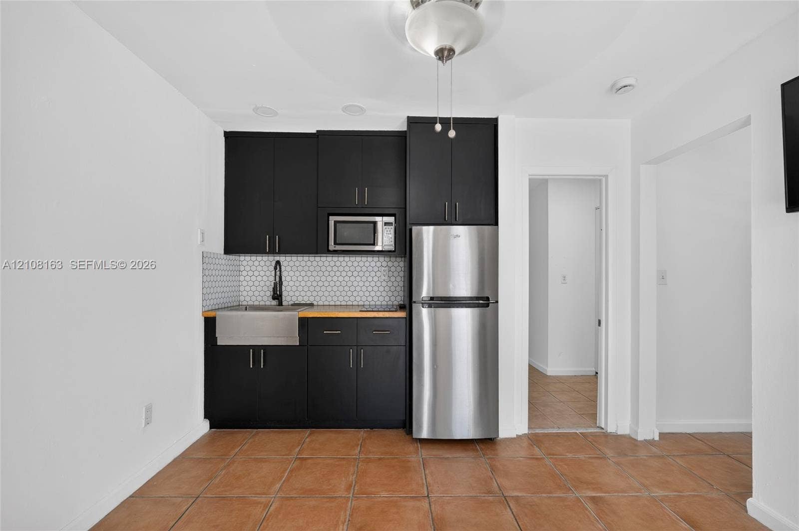11510 SW 5th Street, #1, Sweetwater, Sweetwater, FL 33174 Kitchenette featuring black cabinetry, stainless steel refrigerator, apron-front sink, hexagon tile backsplash, and tile flooring