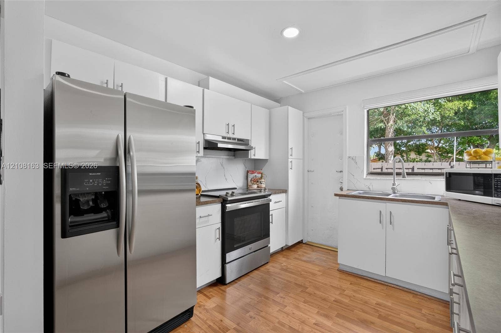 11510 SW 5th Street, #1, Sweetwater, Sweetwater, FL 33174 Kitchen featuring white cabinetry, stainless steel appliances, wood-finish flooring, a double-basin sink with a gooseneck faucet, and stone-finish backsplash