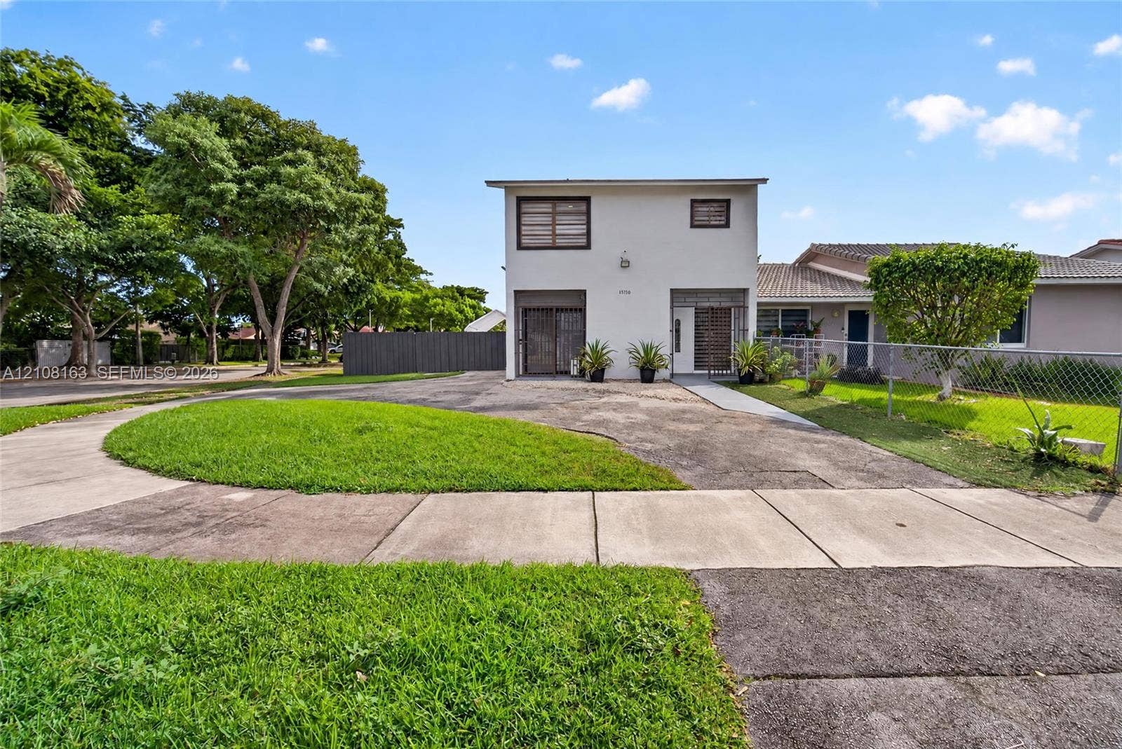11510 SW 5th Street, #1, Sweetwater, Sweetwater, FL 33174 Two-story exterior with a light-toned stucco facade, paved driveway, concrete walkway, and chain-link perimeter fencing