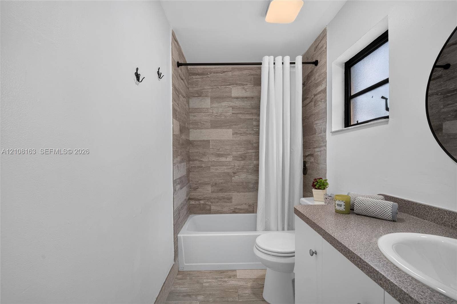 11510 SW 5th Street, #1, Sweetwater, Sweetwater, FL 33174 Bathroom featuring a stone-finish tile tub surround, white vanity cabinet with a stone-finish countertop, undermount sink, and wood-finish tile flooring