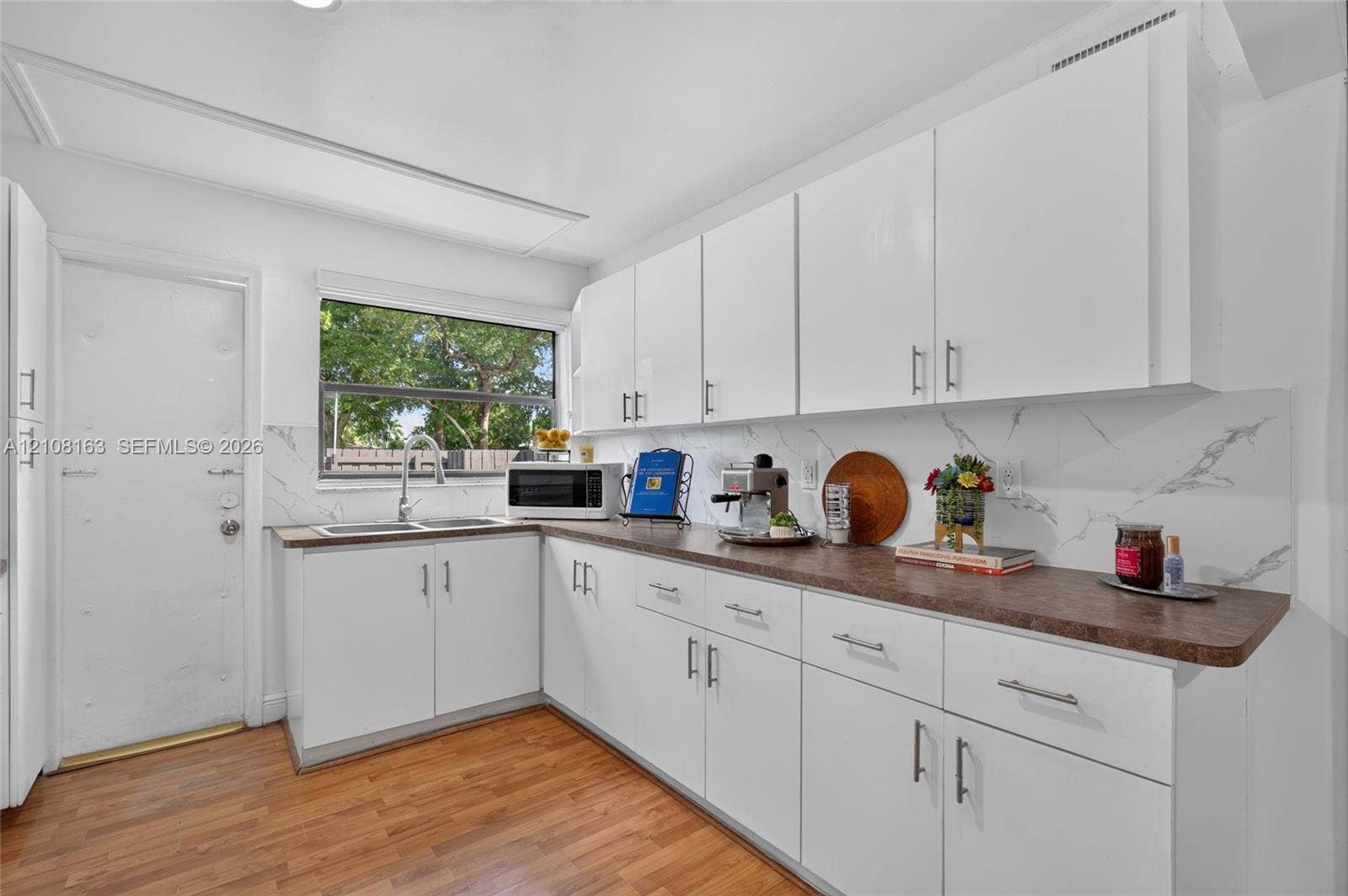 11510 SW 5th Street, #1, Sweetwater, Sweetwater, FL 33174 Kitchen featuring white cabinetry, wood-finish flooring, dark-toned countertops, and a dual-basin stainless steel sink with a stone-patterned backsplash
